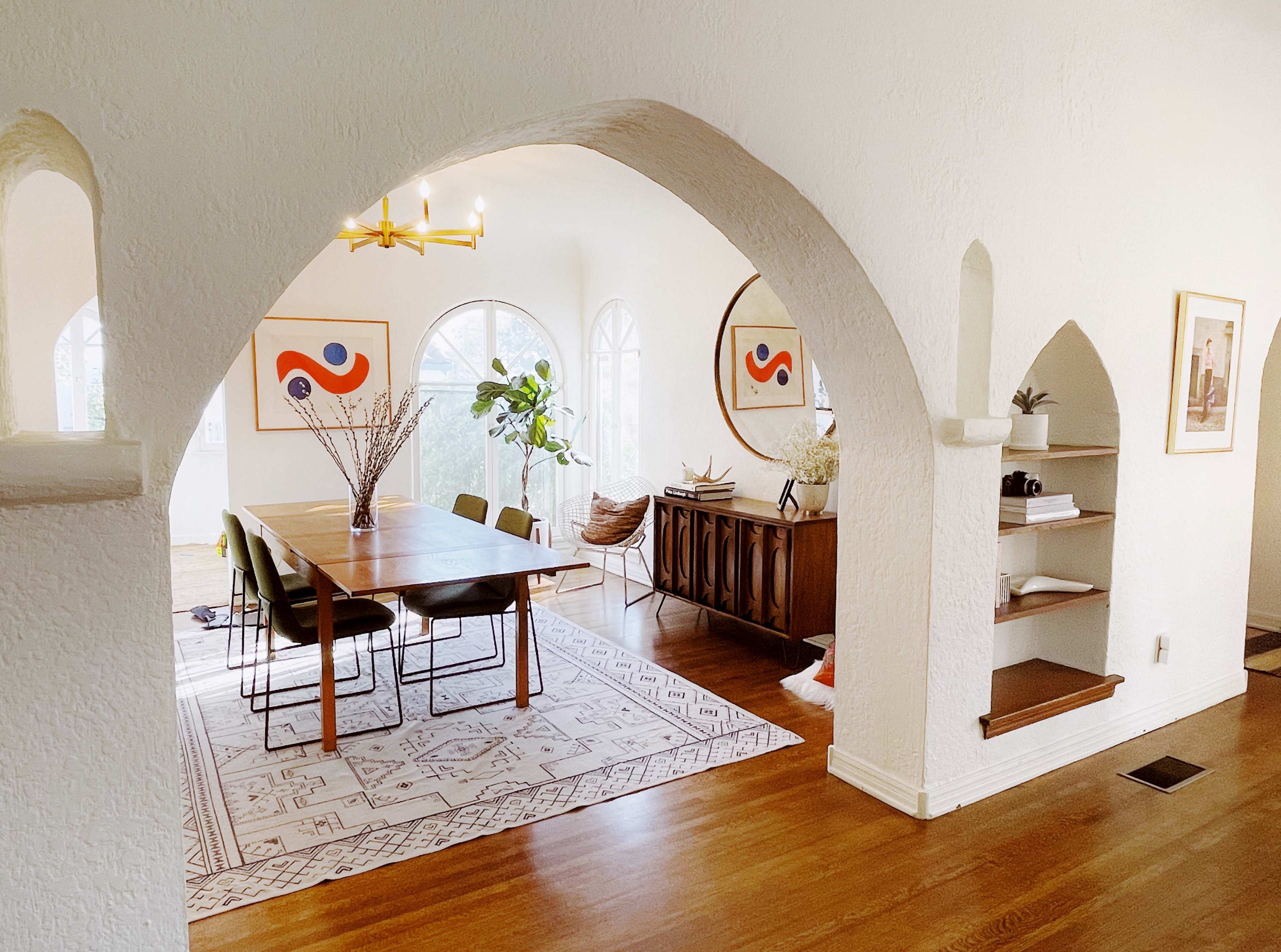A dining area with a wooden table surrounded by chairs, framed art on the walls, and a sideboard, all within an archway entrance.