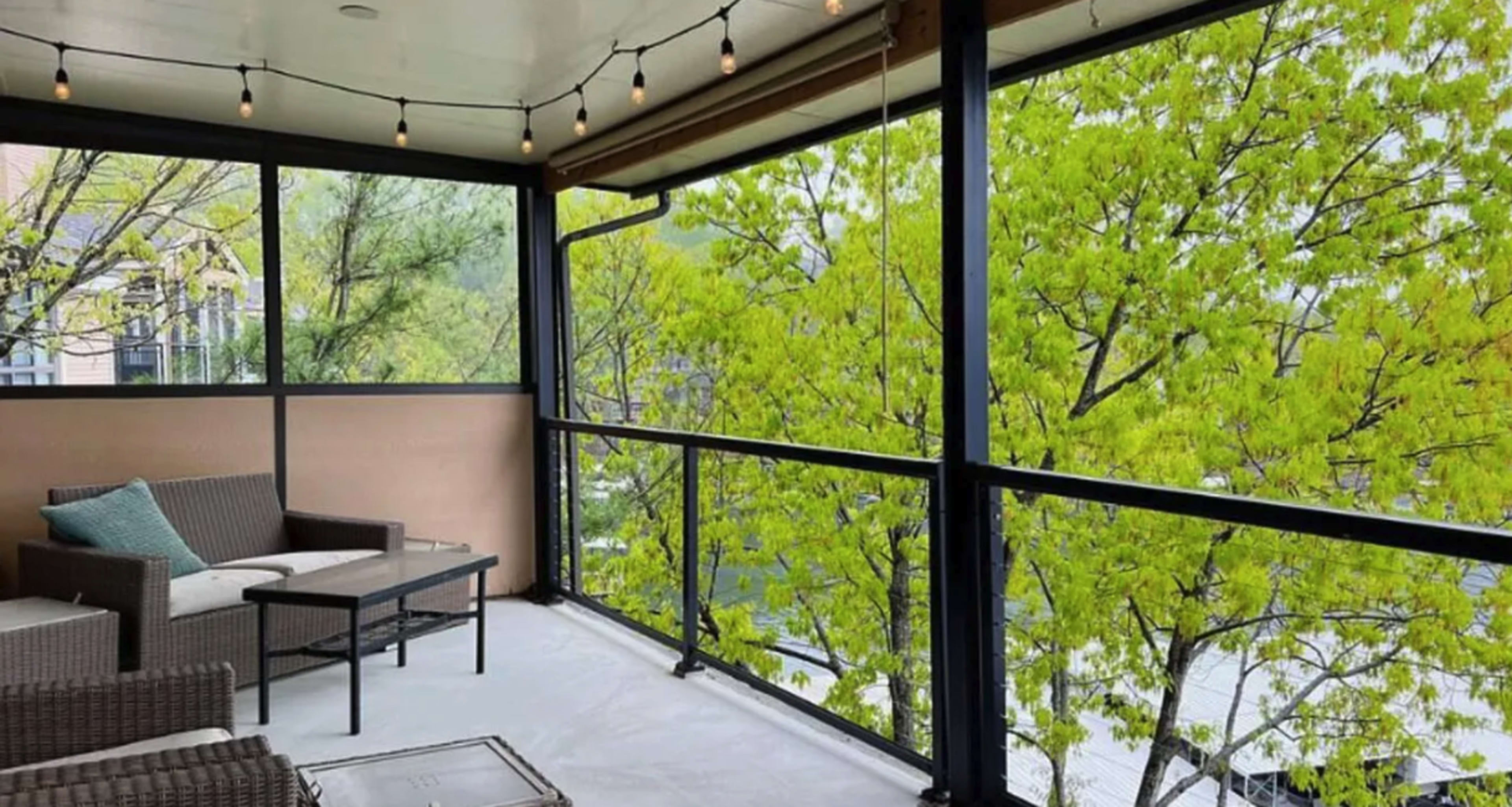 A covered balcony with modern furniture overlooking vibrant green trees.