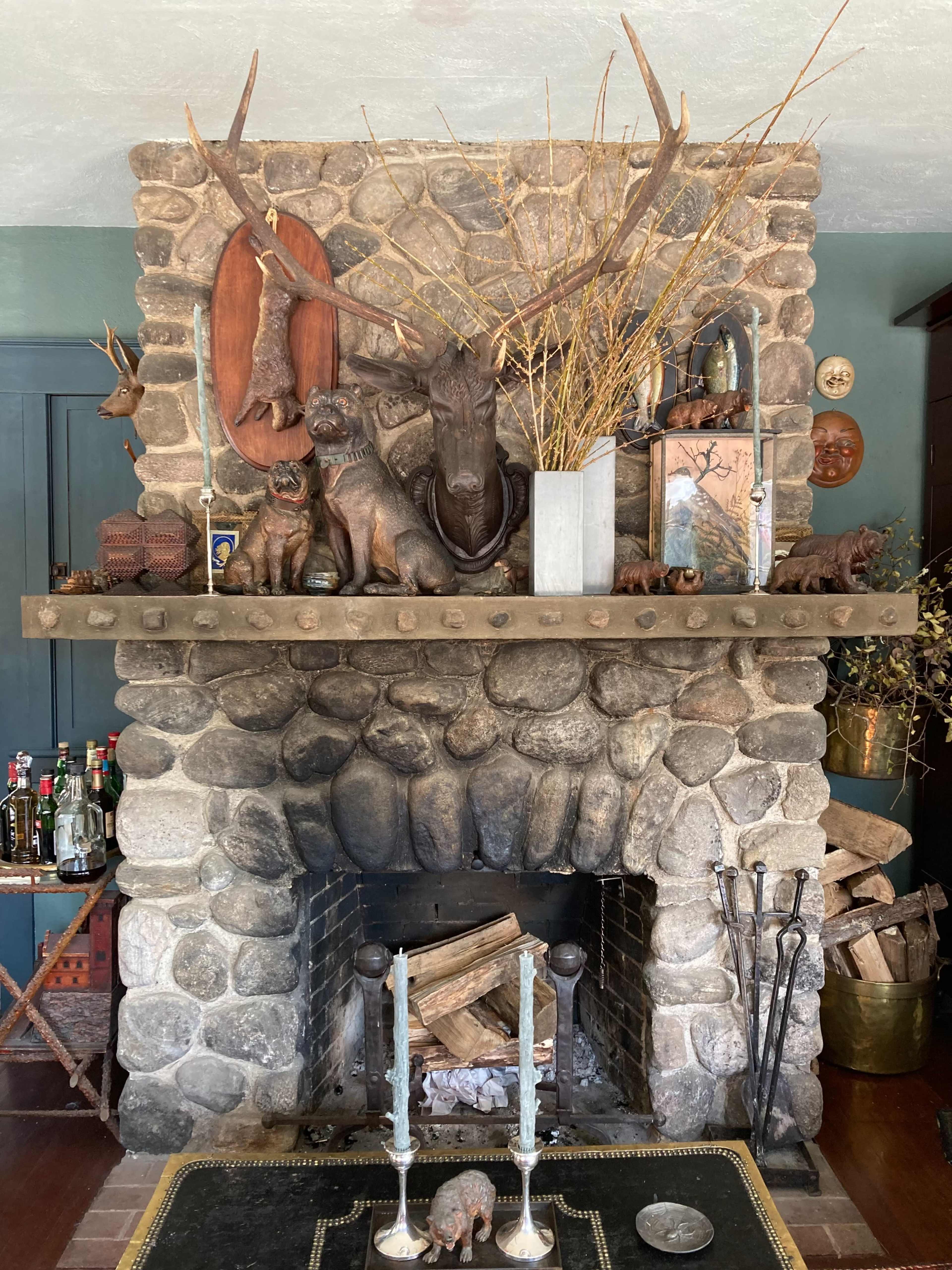 A stone fireplace mantel adorned with mounted animal heads, decorative animal figures, and dried branches.