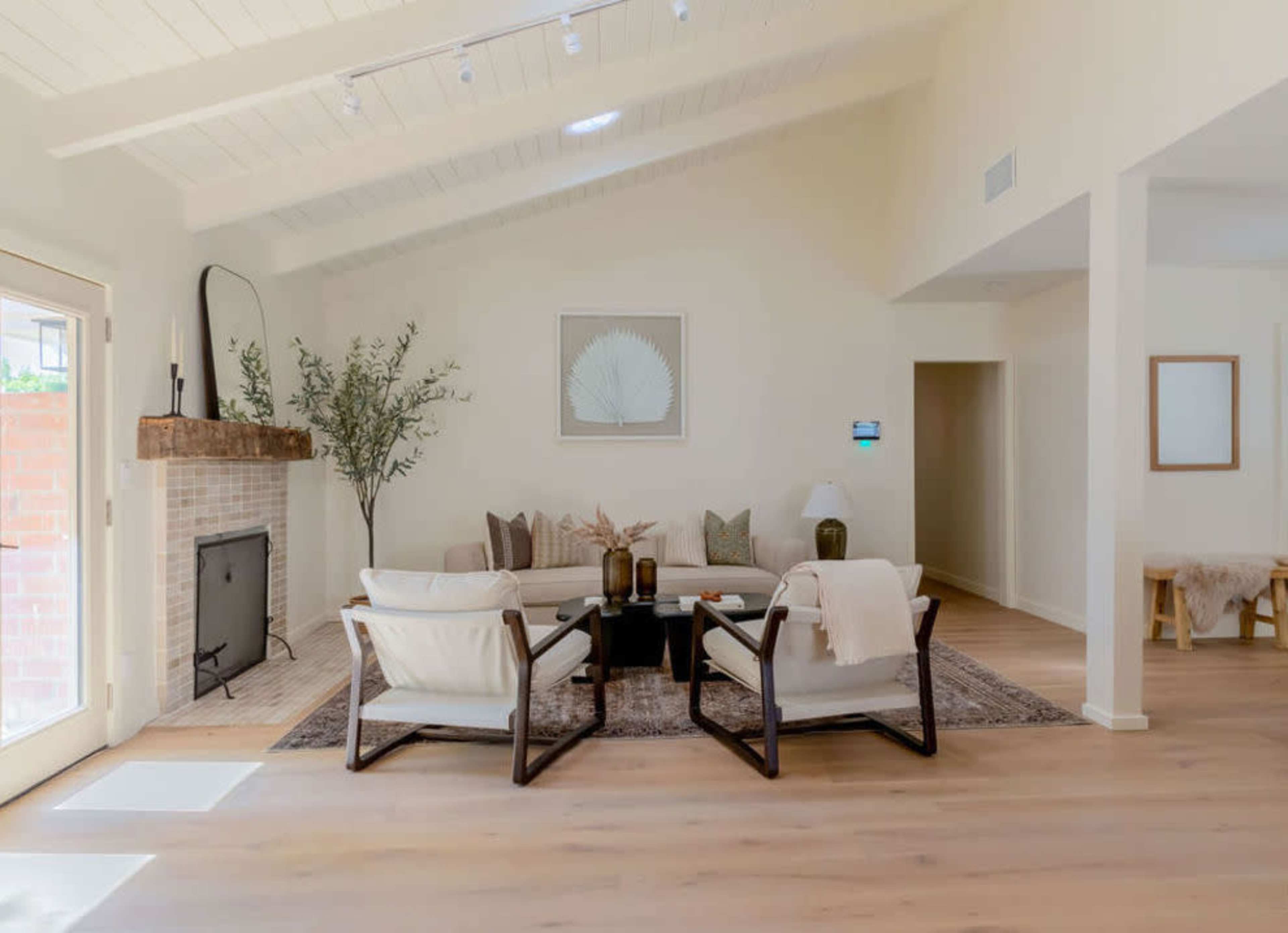The image shows a bright living room featuring a sofa, two armchairs, a coffee table, and a decorative fireplace with a wooden mantel.