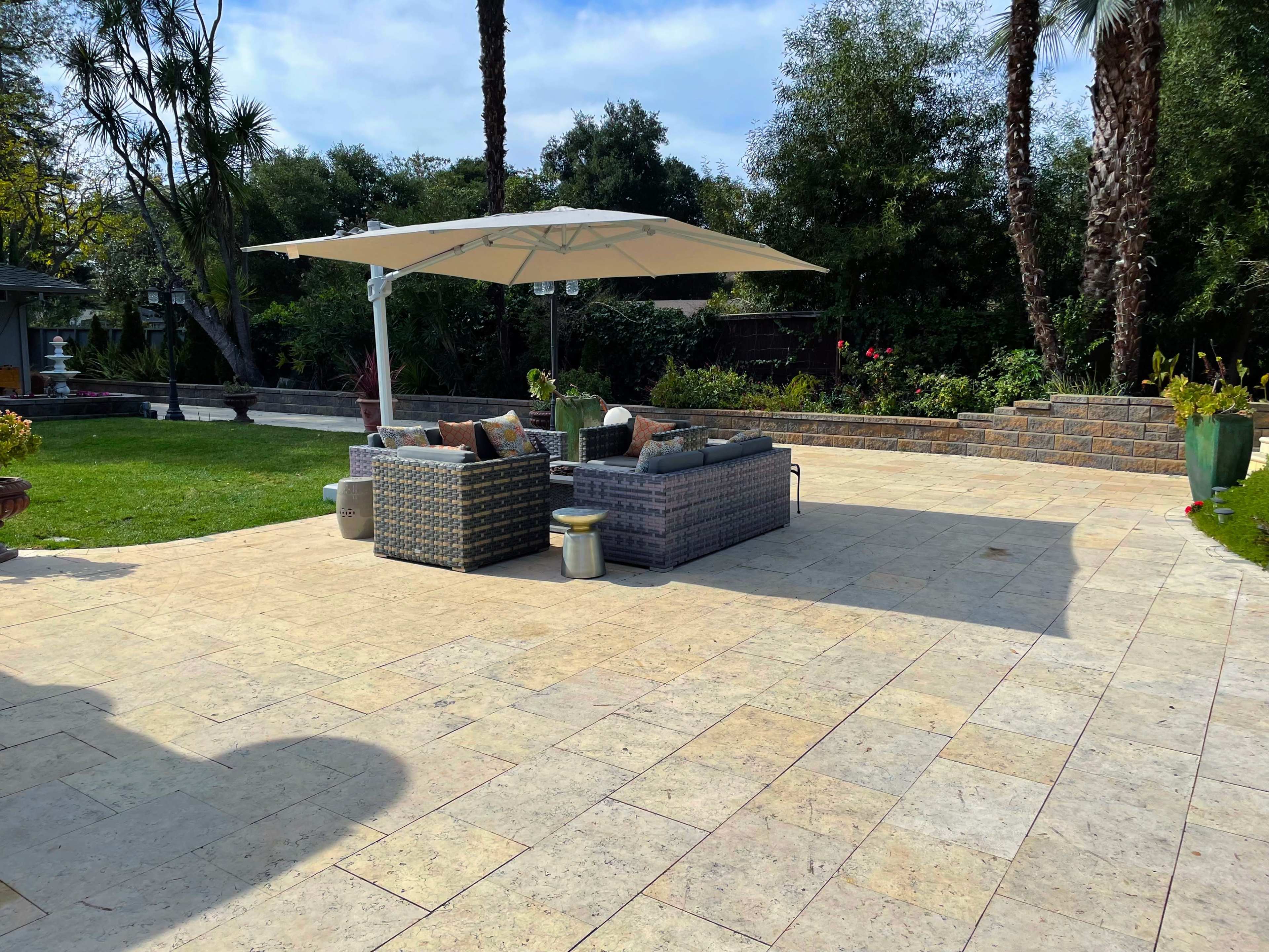 A landscaped outdoor area with a seating arrangement under a large umbrella, surrounded by greenery and decorative plants.