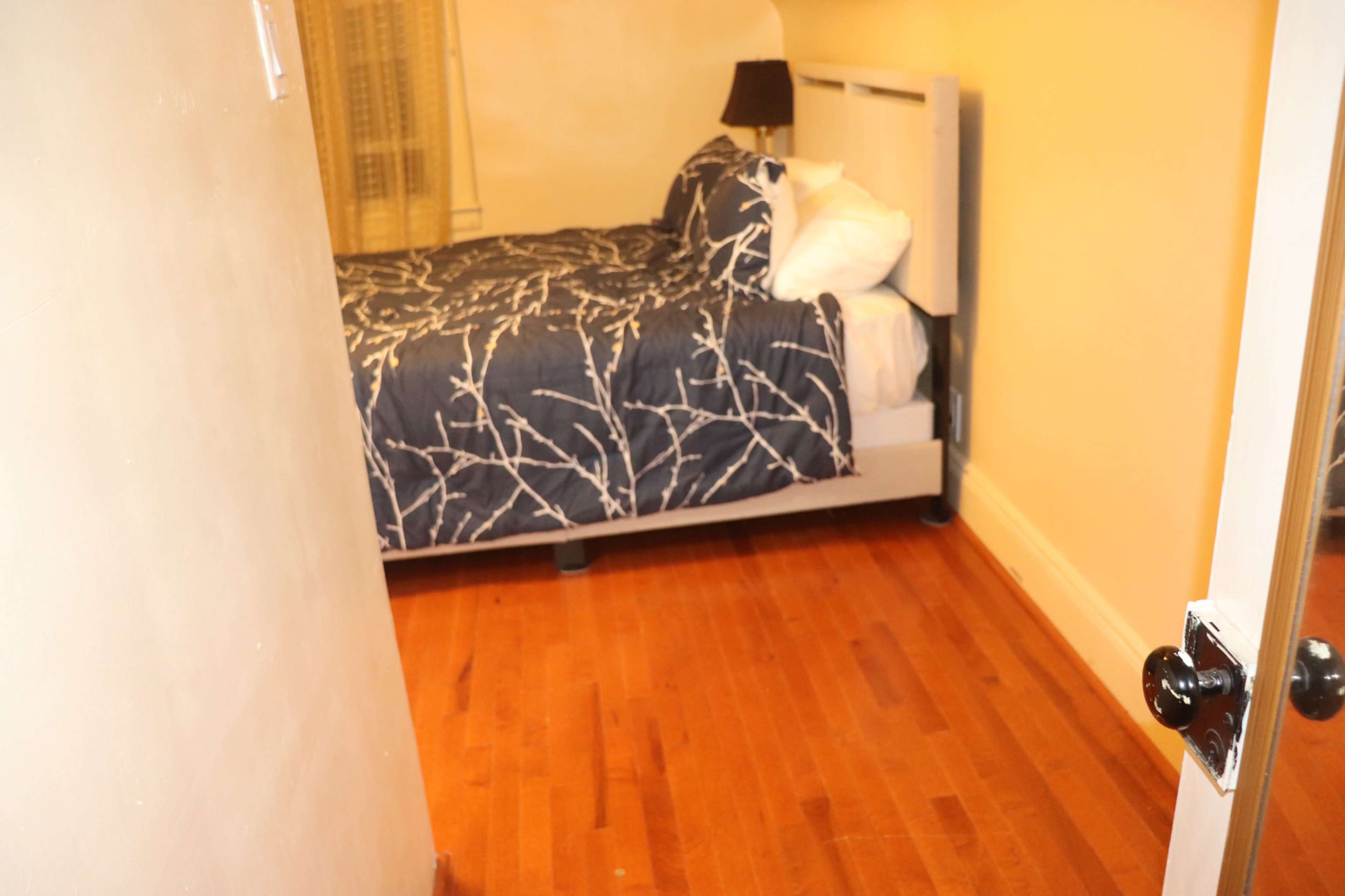 A small bedroom with a bed covered in a dark patterned blanket and a lamp on a bedside table.