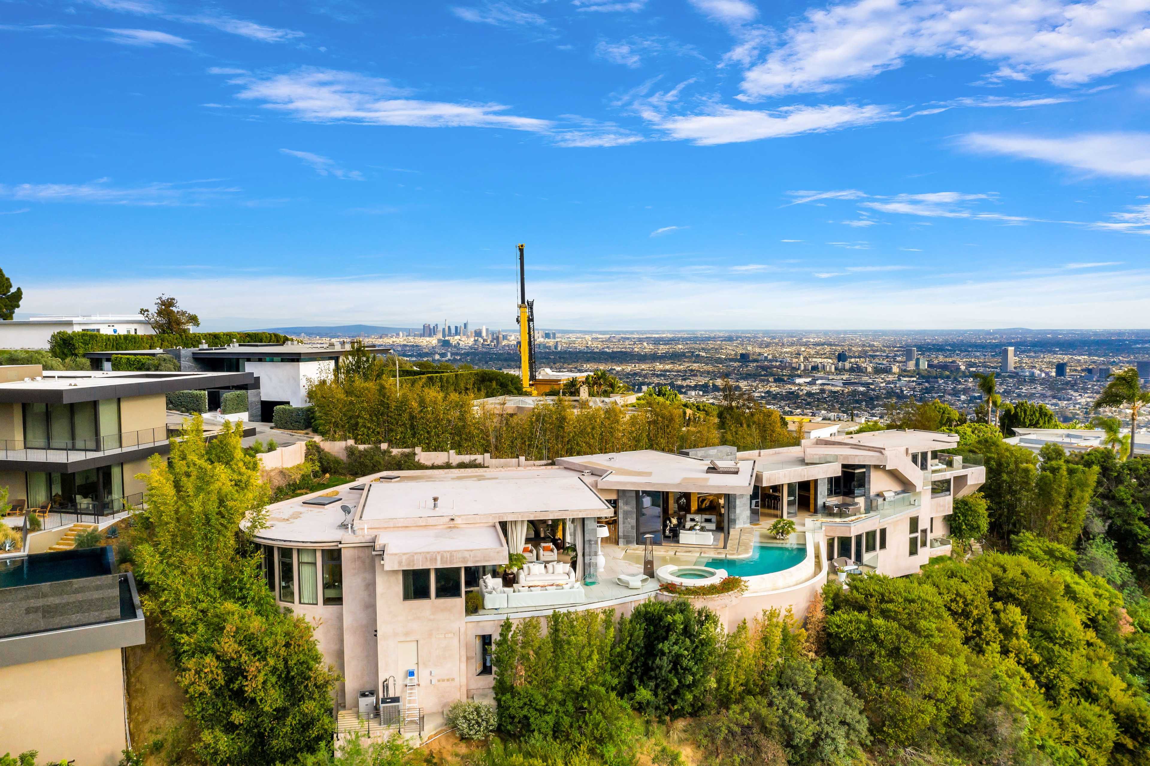A luxurious hillside house with a curved design overlooks a sprawling cityscape under a clear blue sky.