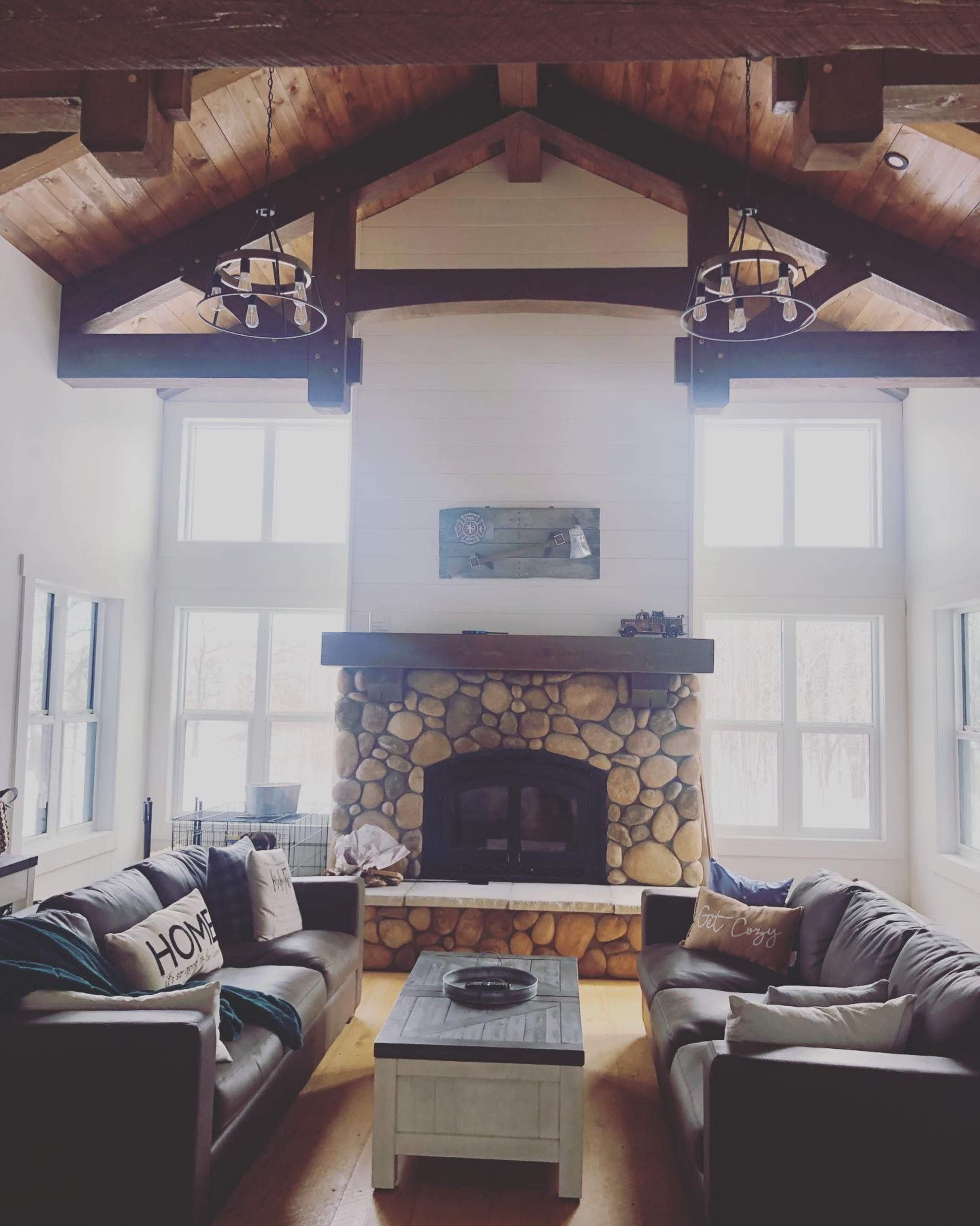 A spacious living room with a stone fireplace, two dark leather sofas, and large windows letting in natural light.