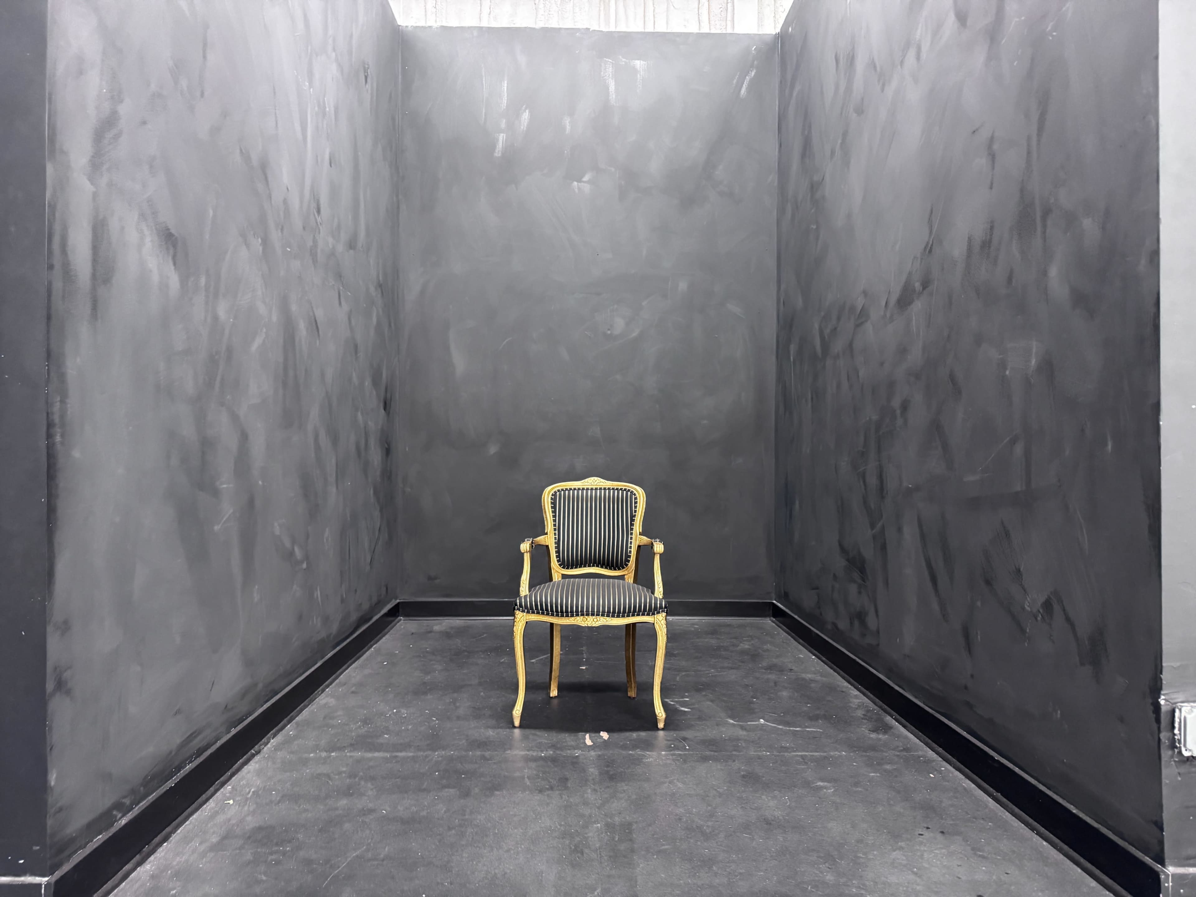 A yellow-striped chair stands alone in a large, empty room with black walls.
