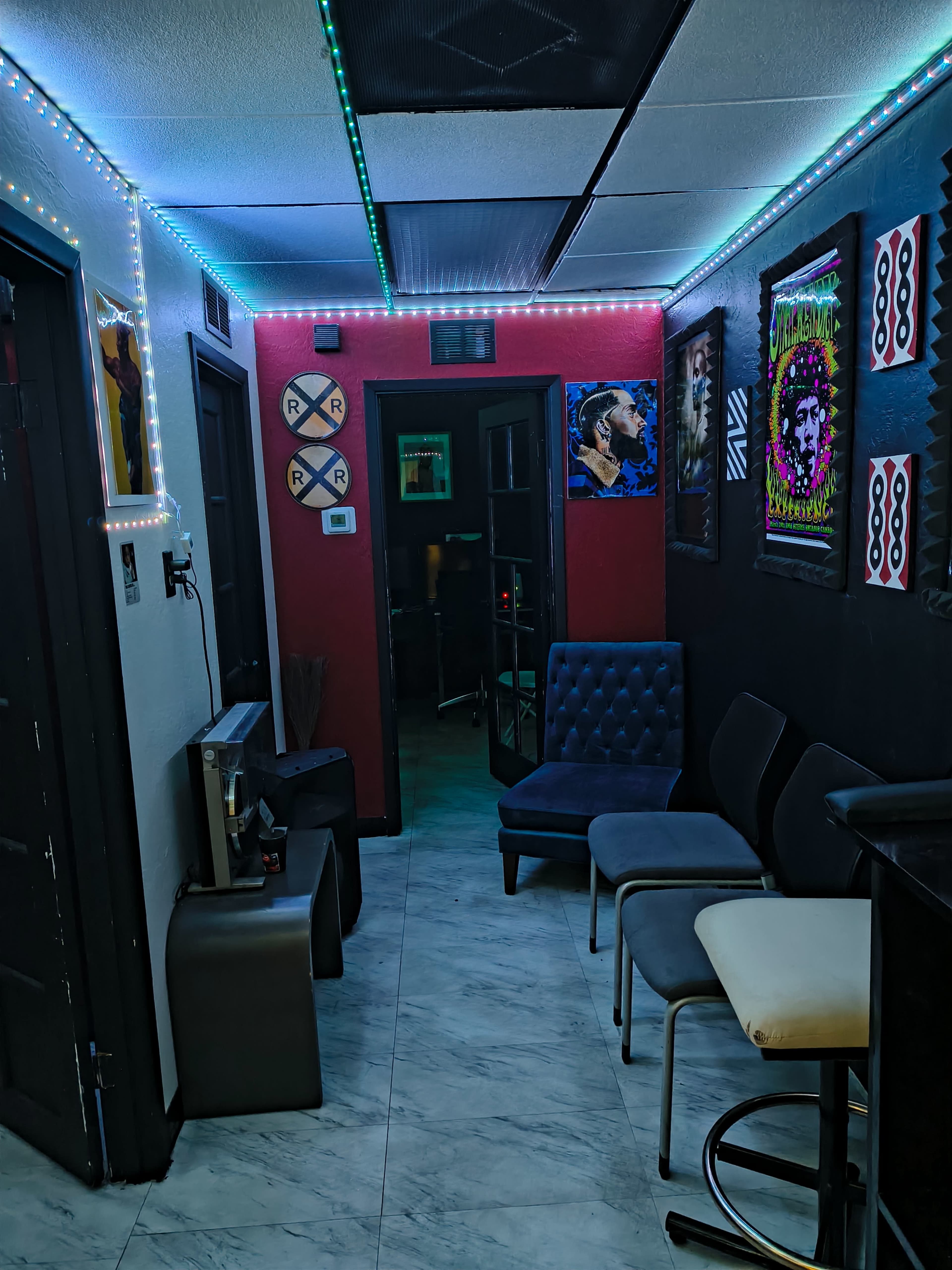 The image shows a narrow hallway adorned with colorful LED lights, leading to entranceways of various rooms decorated with framed posters and art.