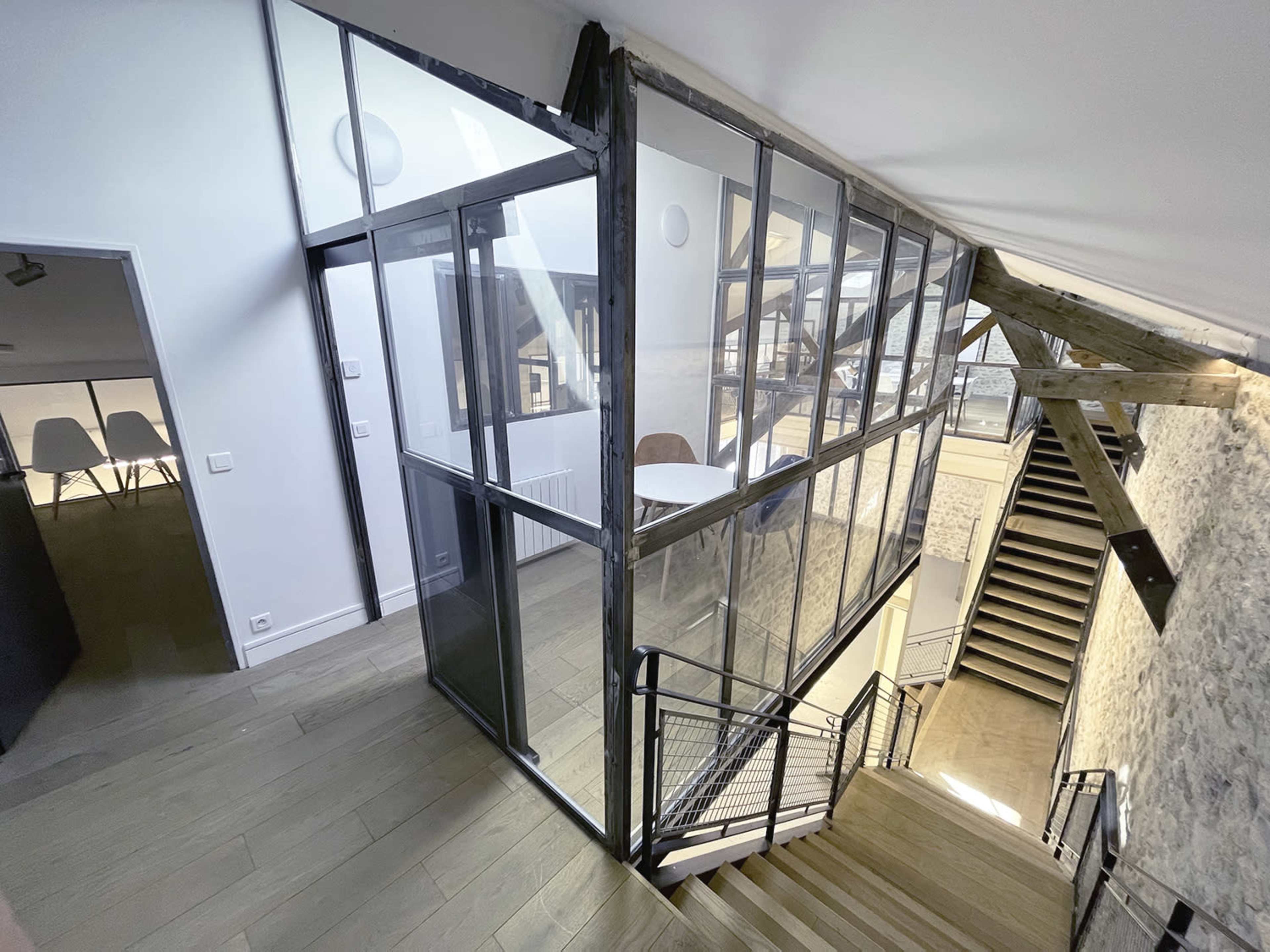 A modern staircase with a glass and metal partition separating different areas of a contemporary interior space featuring exposed stone walls and wooden beams.