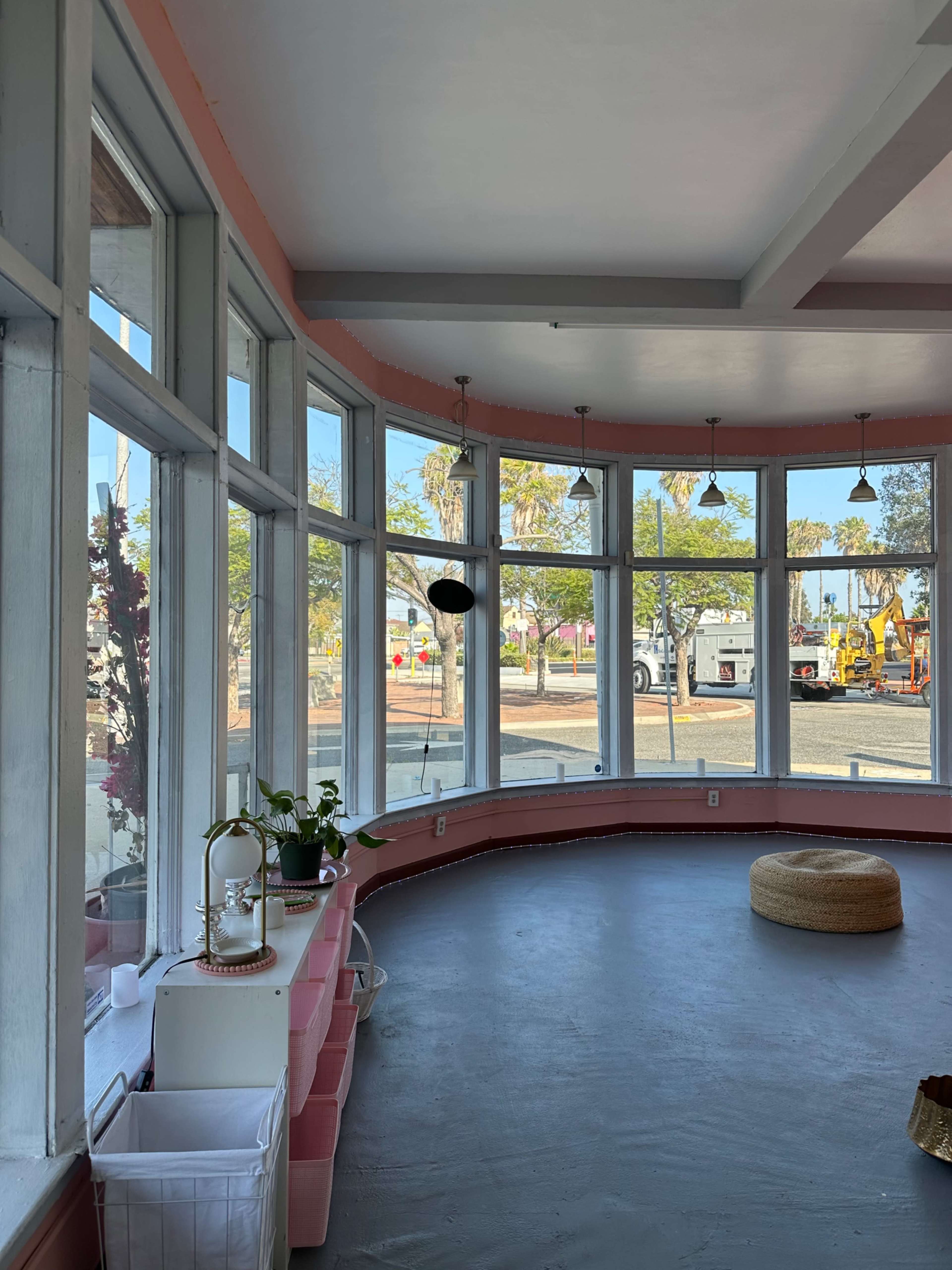 The image shows a bright interior space with large windows, a curved seating area, and plants, overlooking an outdoor scene with construction equipment.