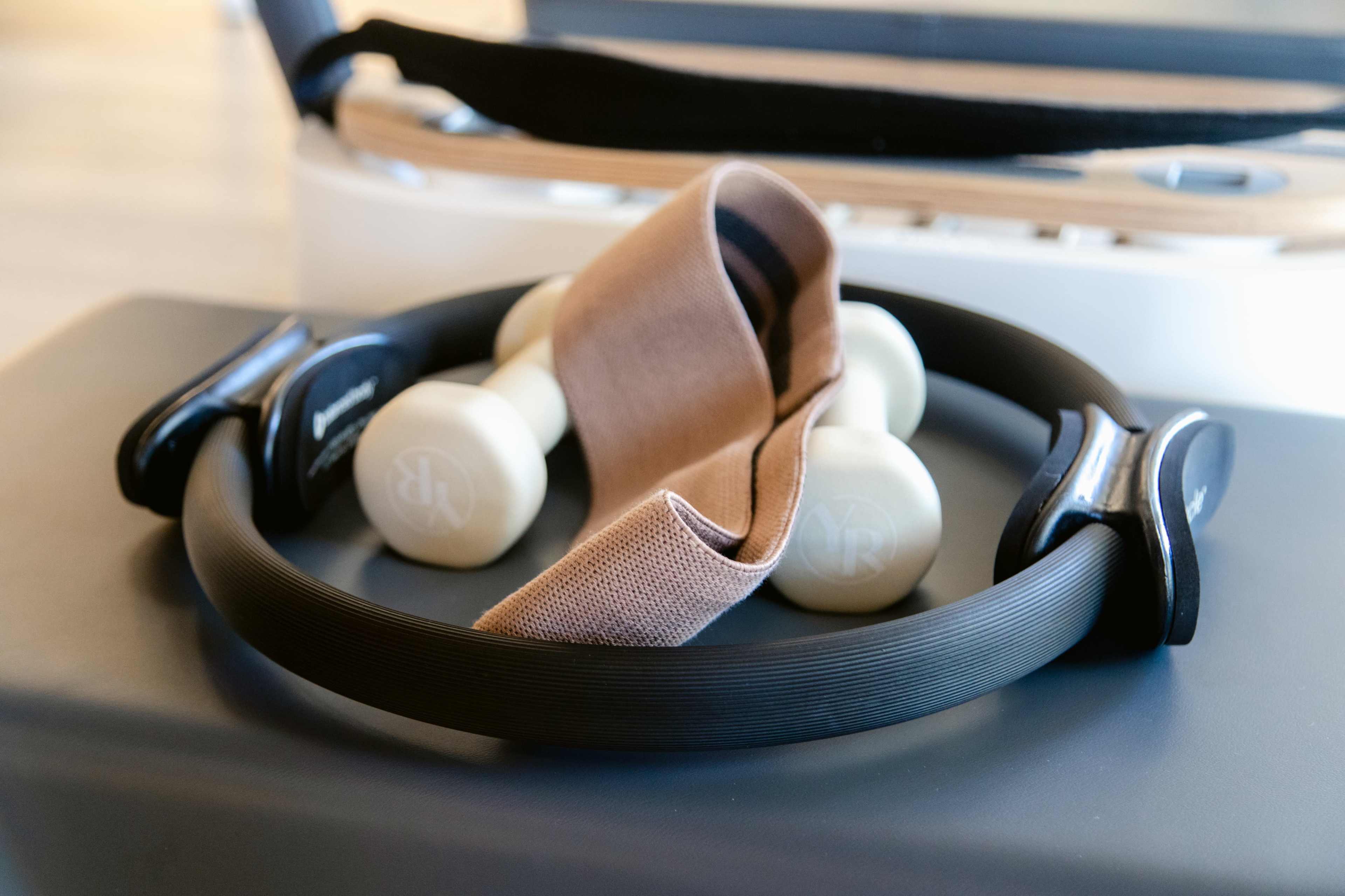 A black resistance ring and a pair of light-colored dumbbells are resting on a gray exercise mat.
