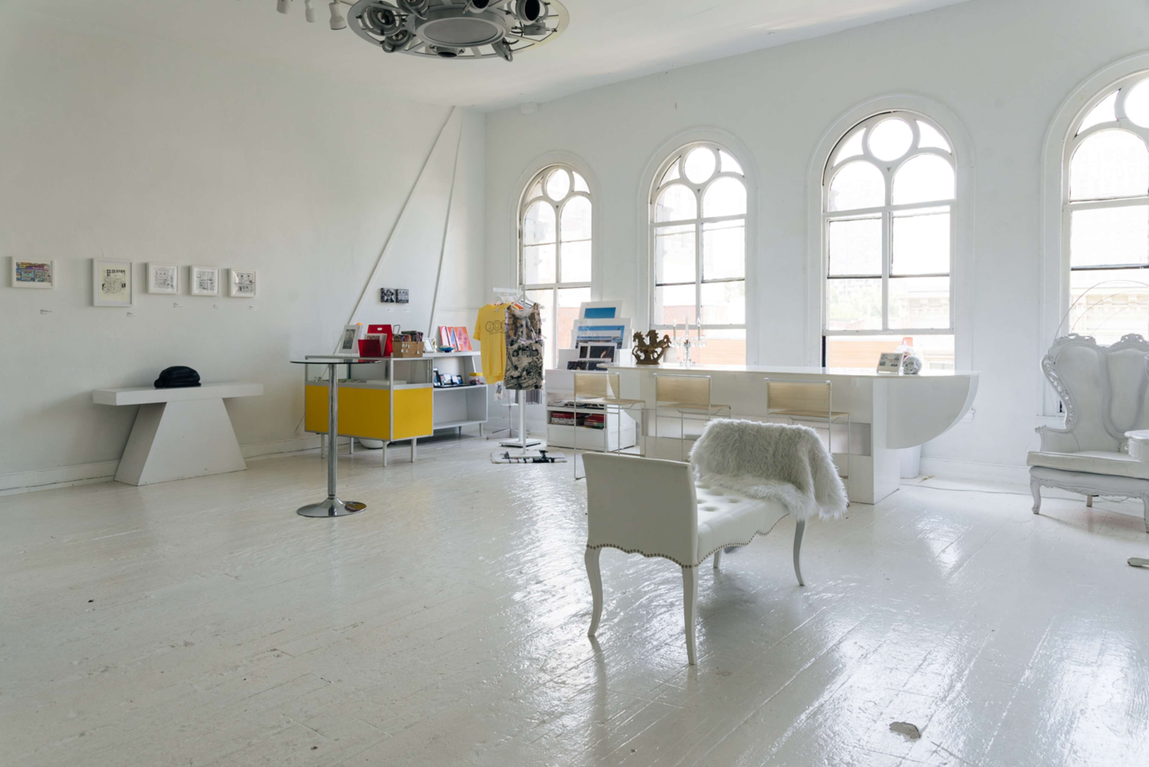 A bright, airy room with large arched windows, featuring minimalist furniture, including a white chair and a modern display table.
