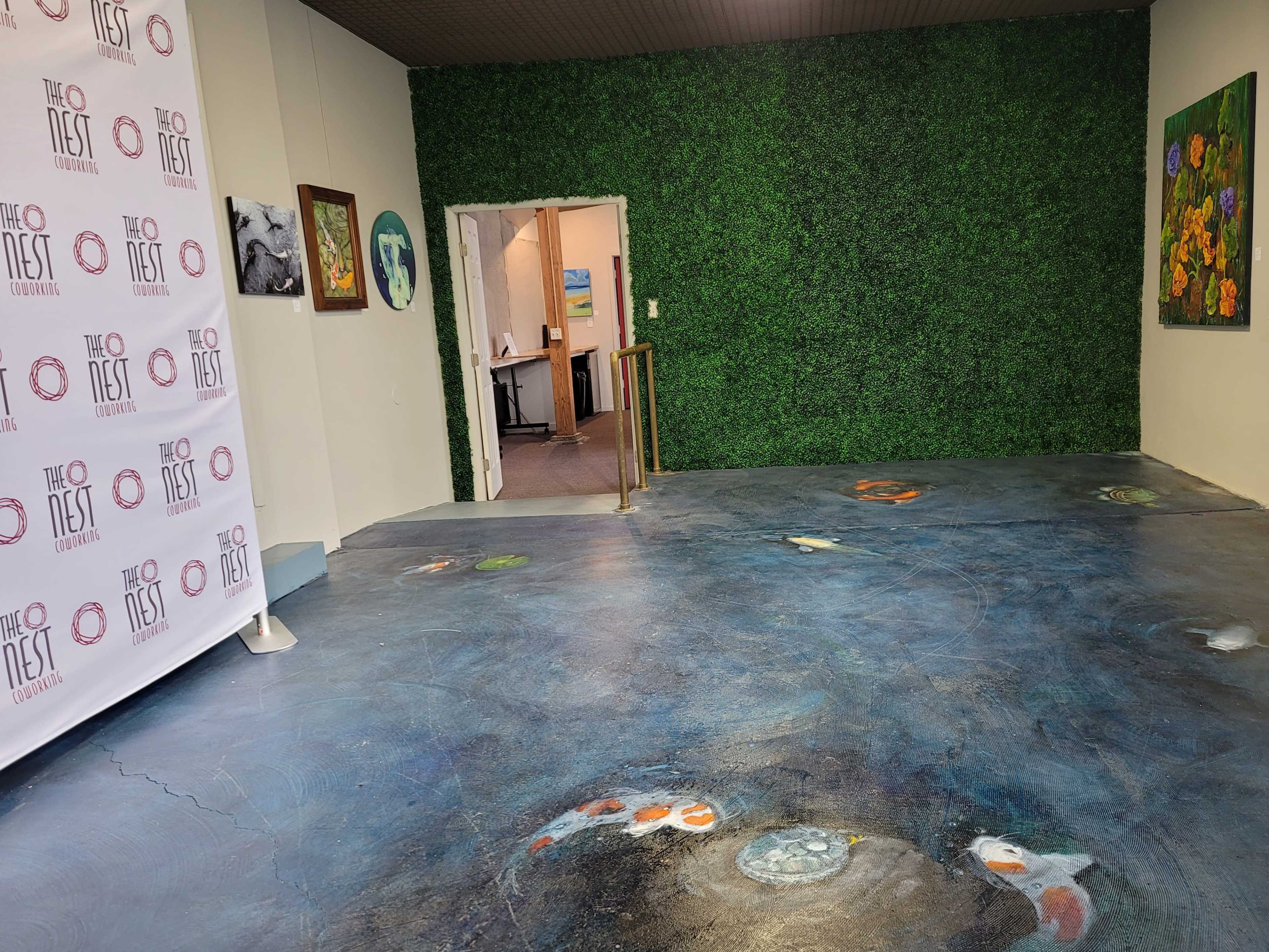 A room with a blue-tinged floor featuring artistic designs and a wall covered in green foliage, along with a banner for "The Nest" on one side.