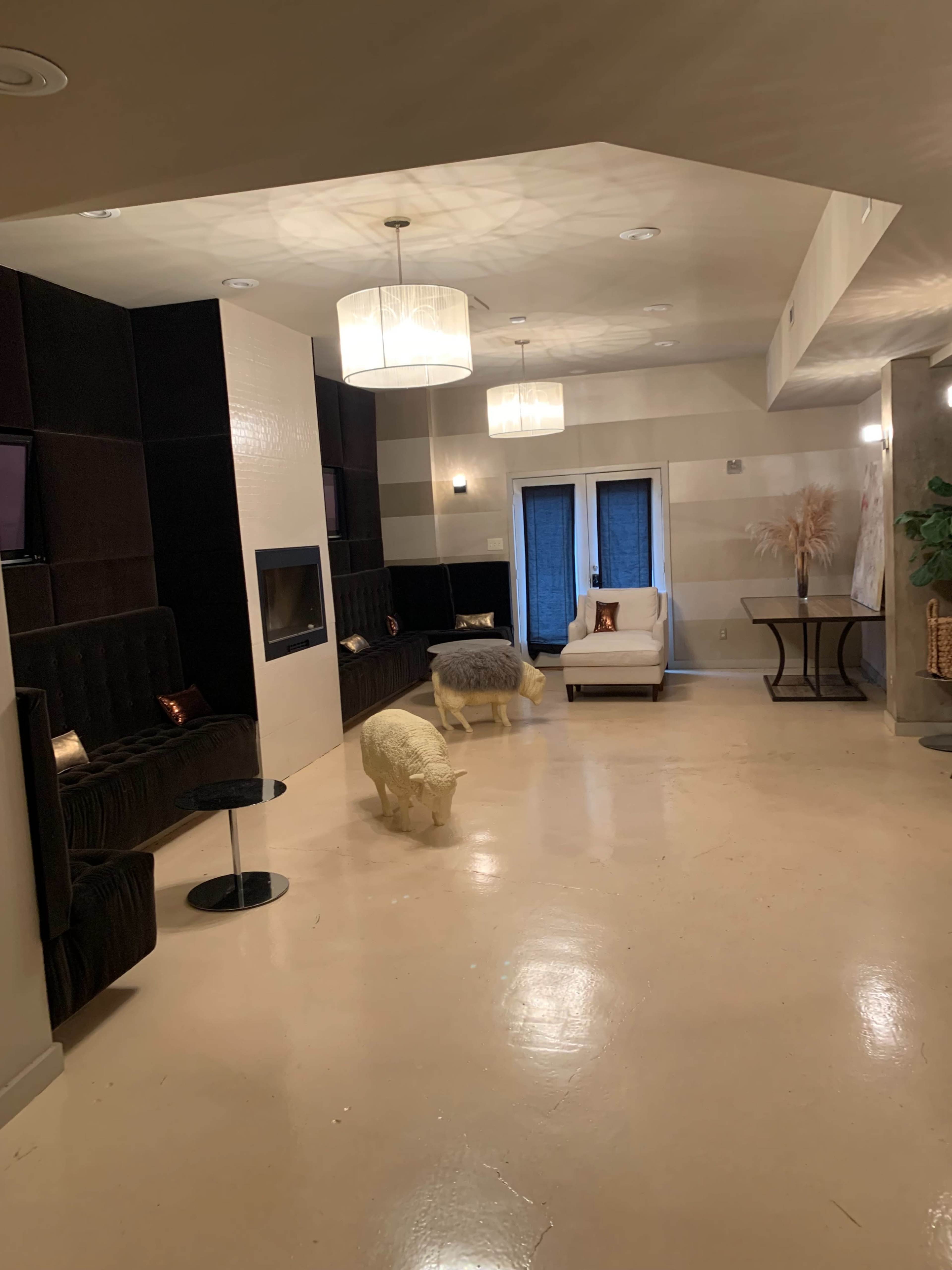 A spacious, modern living area featuring a sectional couch, a television mounted on the wall, a white armchair, and decorative lighting fixtures hanging from the ceiling.