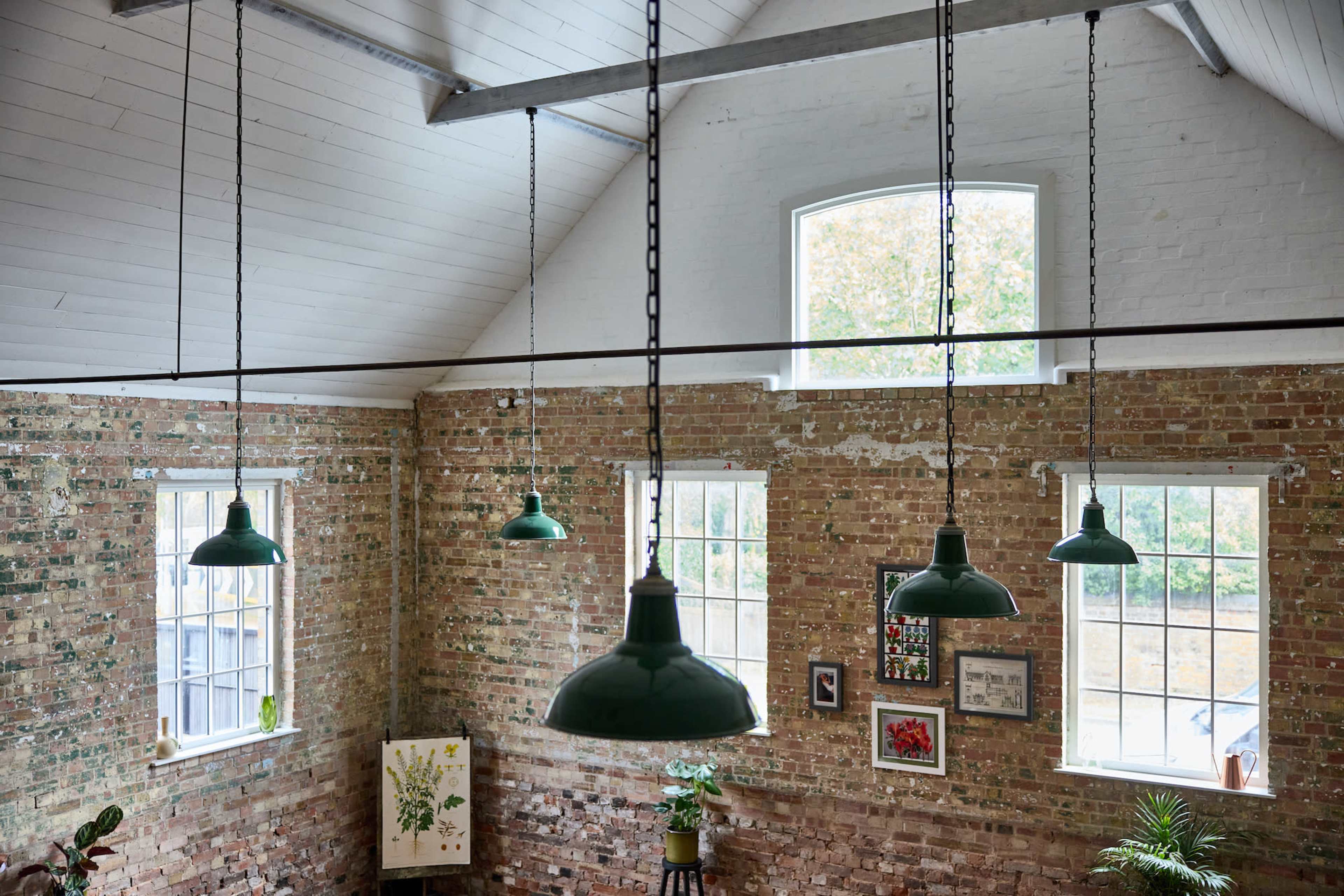 A spacious room with exposed brick walls, large windows, and green industrial-style pendant lights hanging from the ceiling.