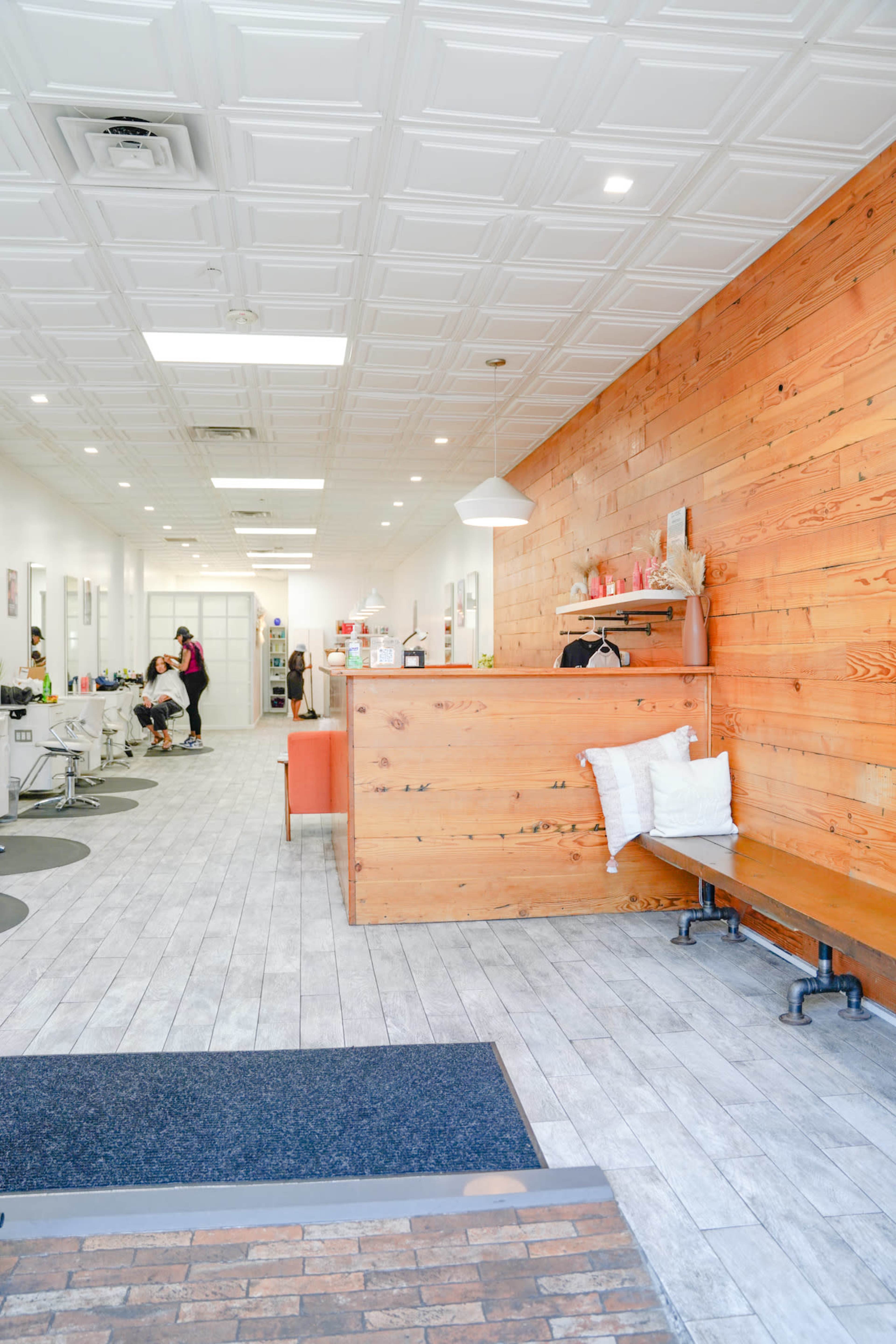 A modern hair salon with wooden accents, light-colored walls, and several salon stations occupied by clients and stylists.