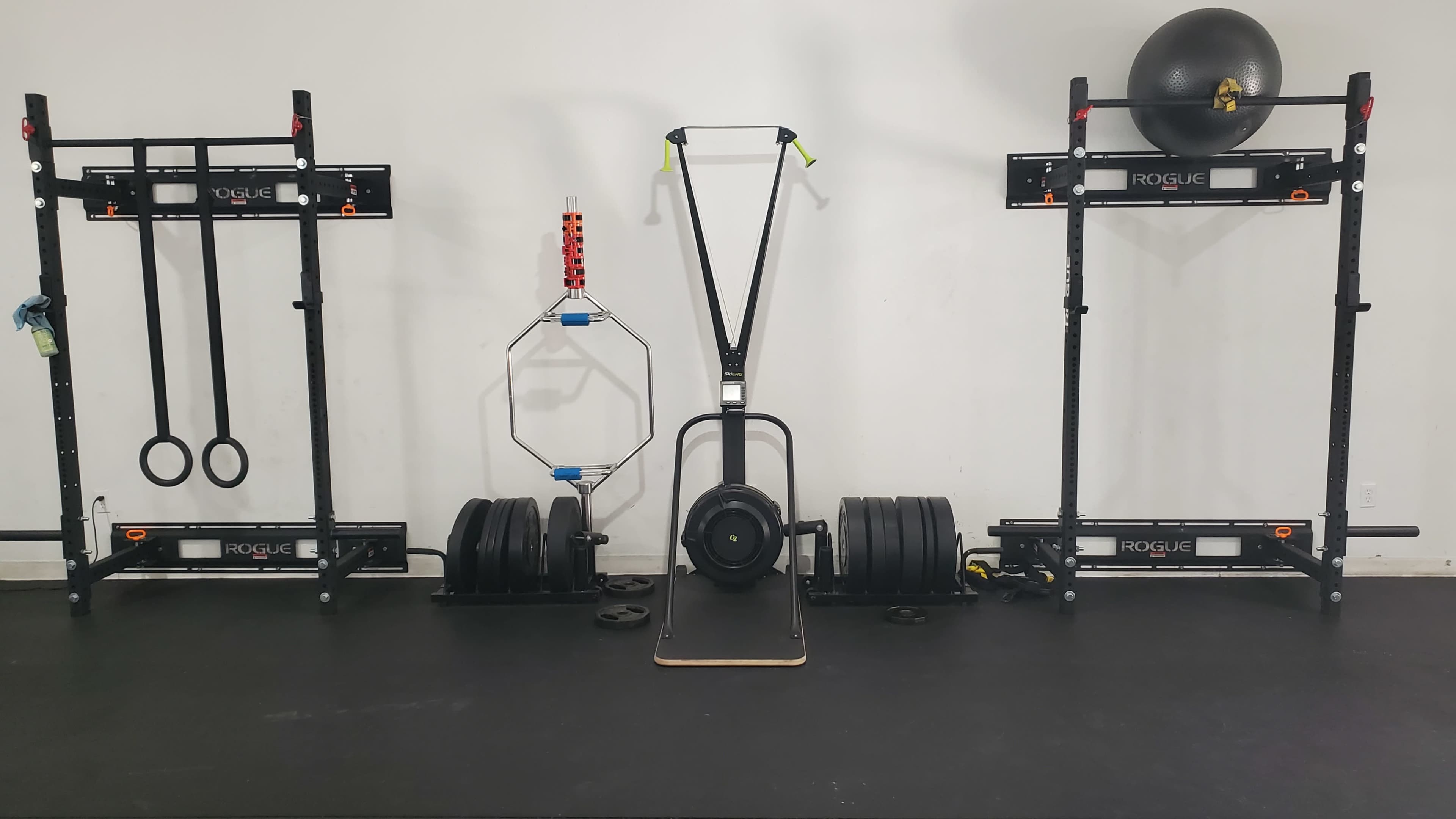 A gym setup featuring a sled push apparatus at the center, flanked by weightlifting racks on both sides, along with various weights and fitness equipment.