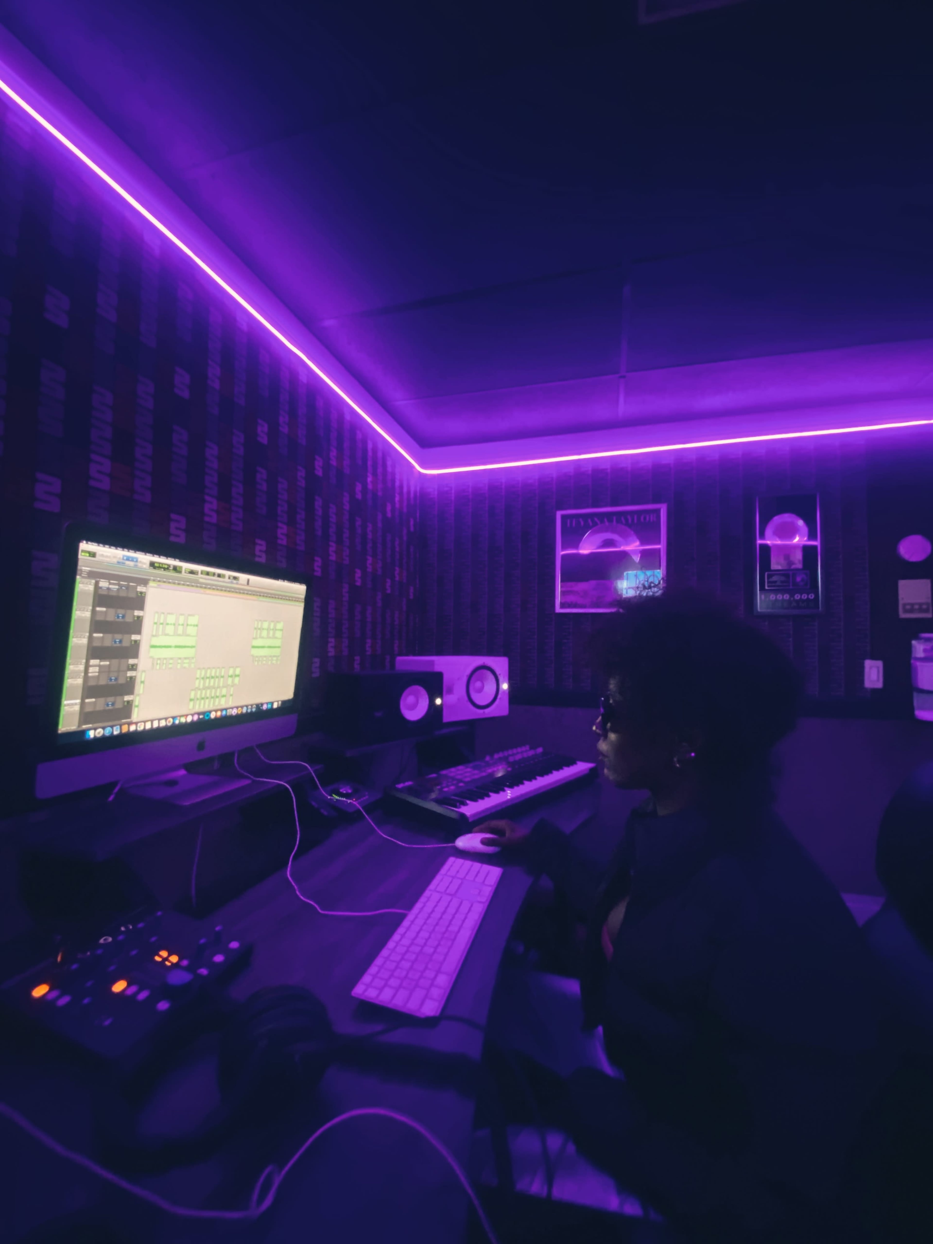 A person works at a computer in a music production studio with purple ambient lighting.