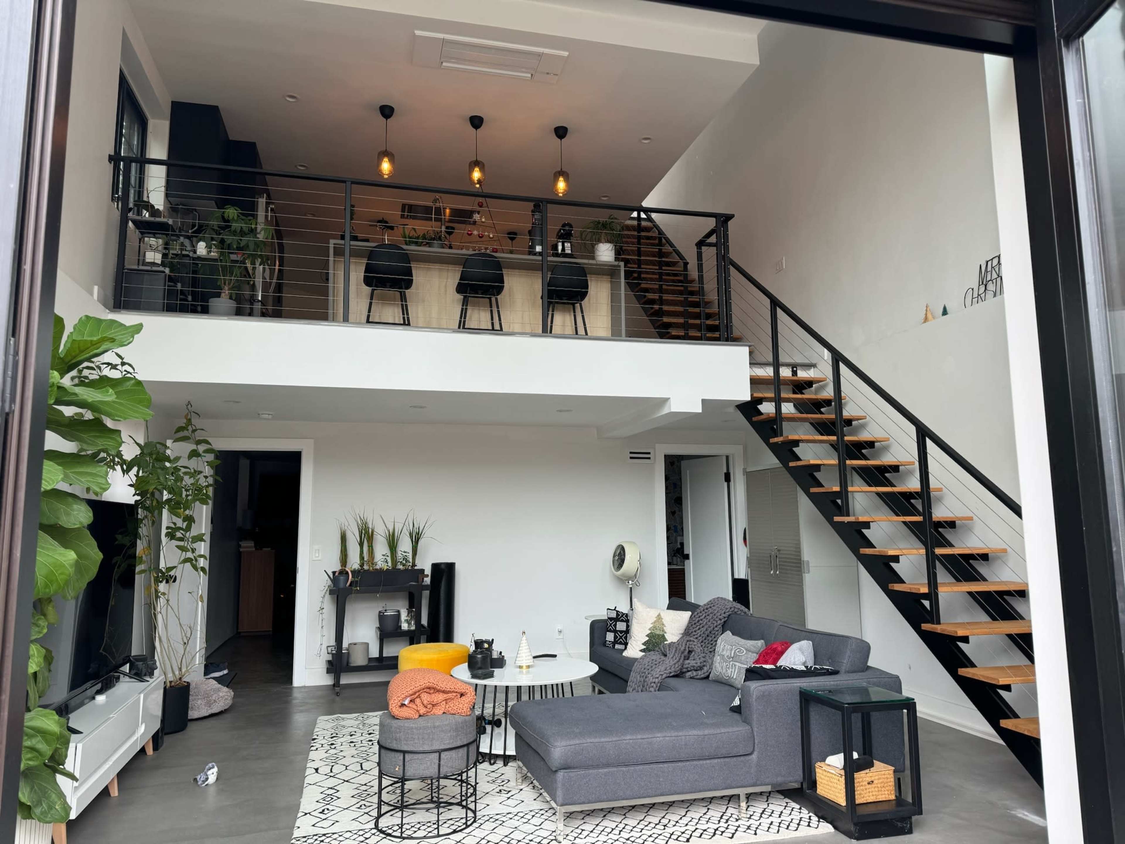 A modern interior space with a two-level layout featuring a living area, a staircase, and a kitchen with bar seating.