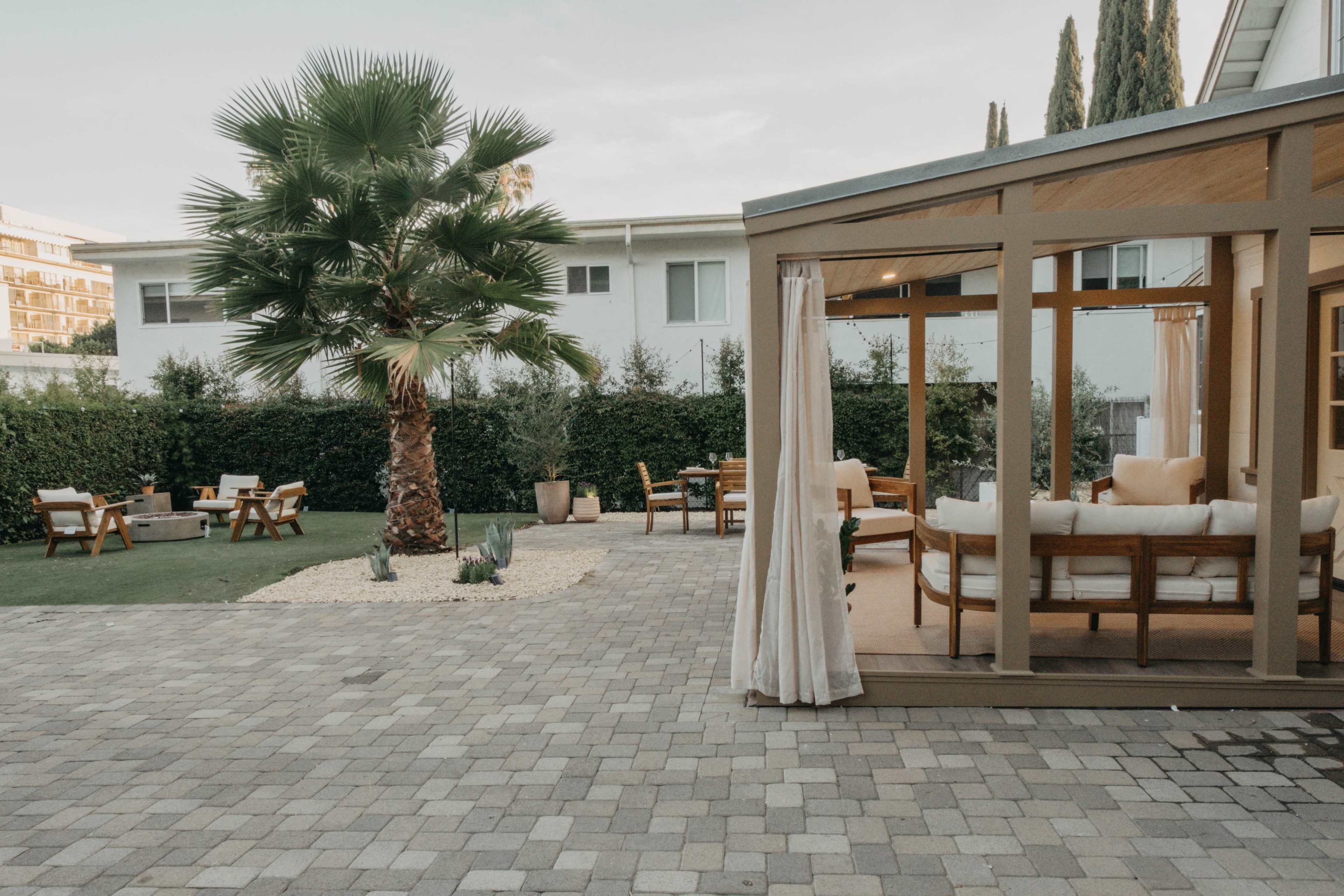The image shows a backyard patio area featuring a wooden gazebo, a palm tree, and outdoor seating arrangements.