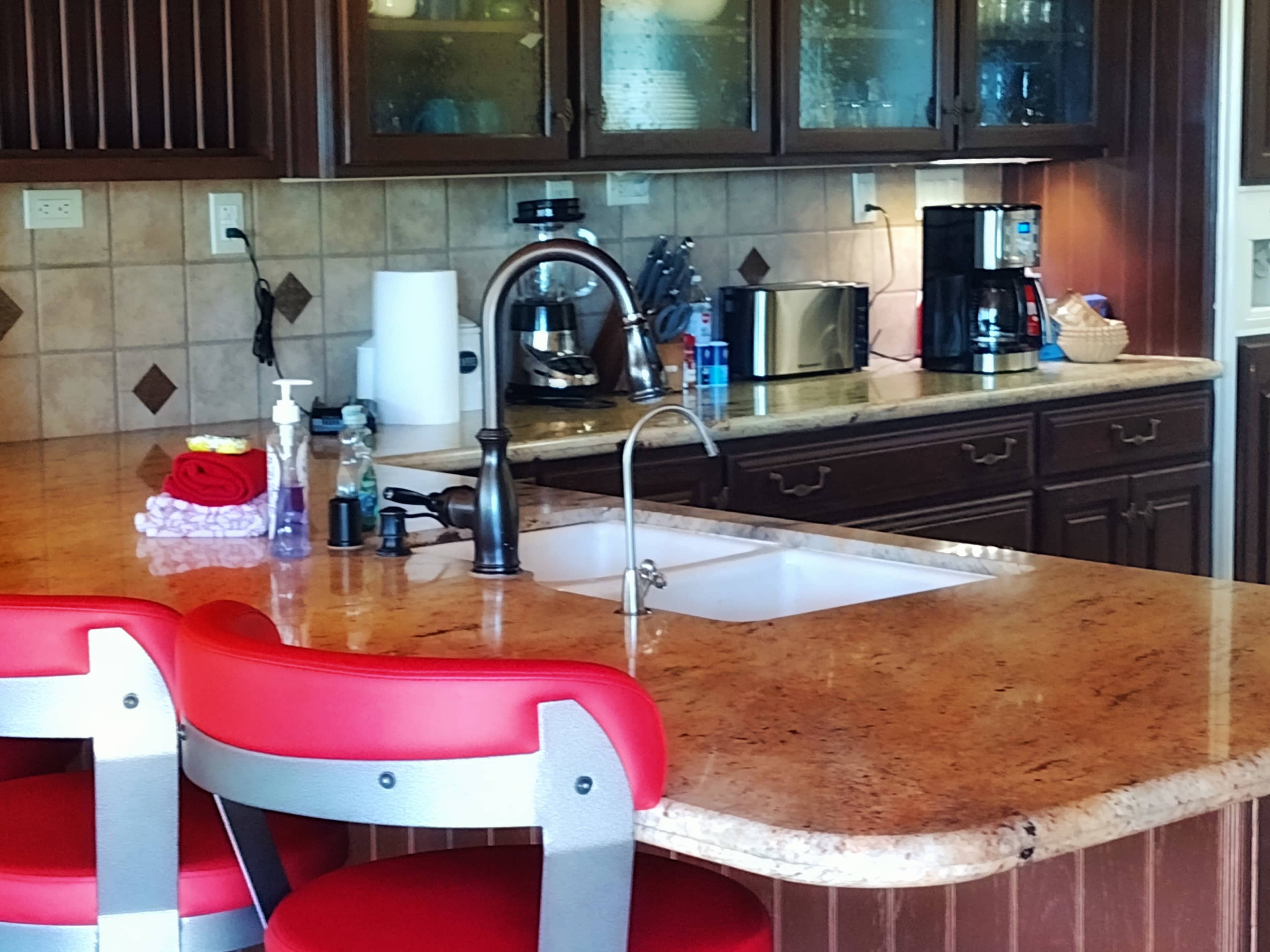 A kitchen with dark wooden cabinets, a granite countertop, and various appliances including a coffee maker, microwave, and dish soap by the sink.