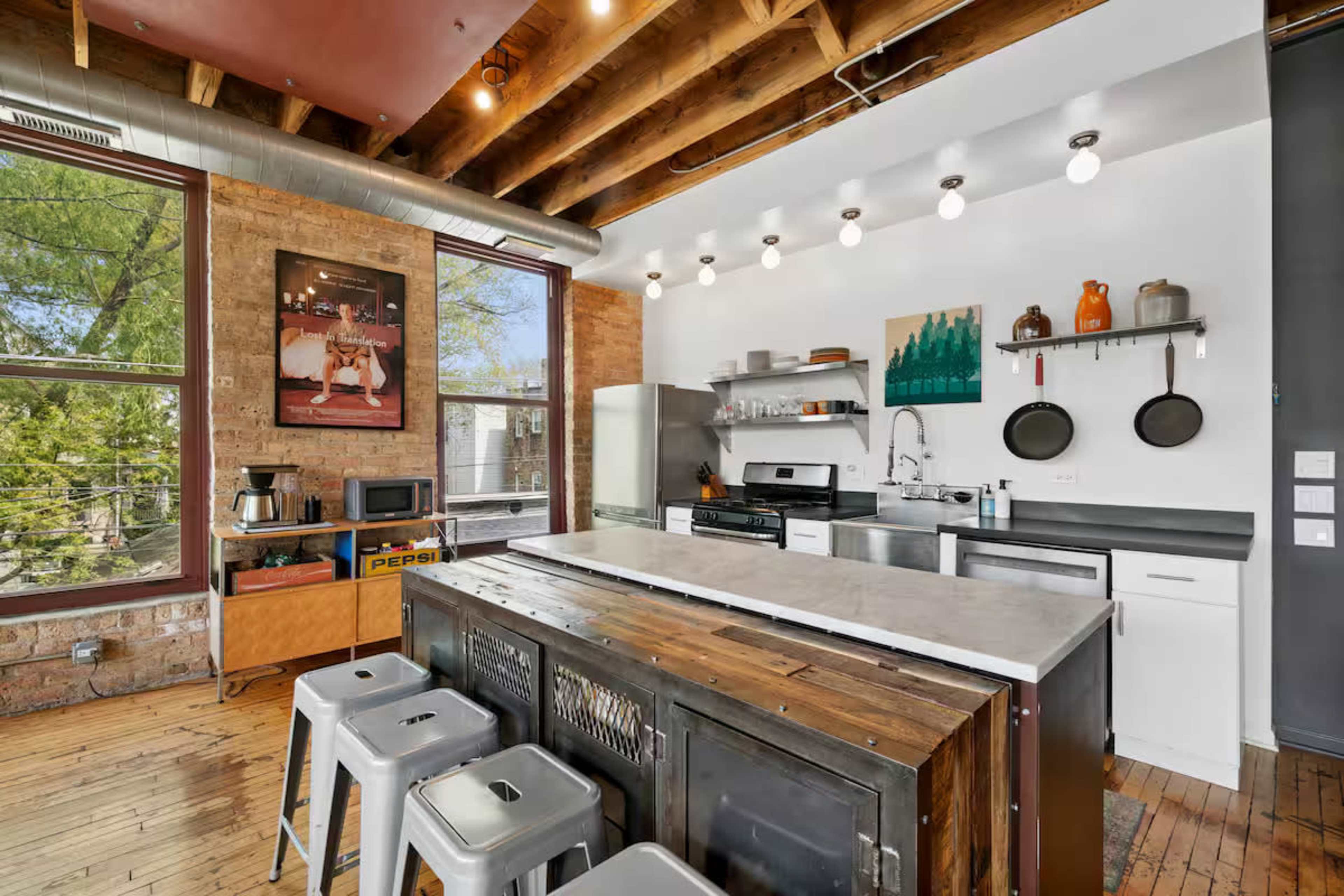 The image shows a modern kitchen with exposed wooden beams, a central island with bar stools, and a mix of stainless steel and wooden cabinetry.