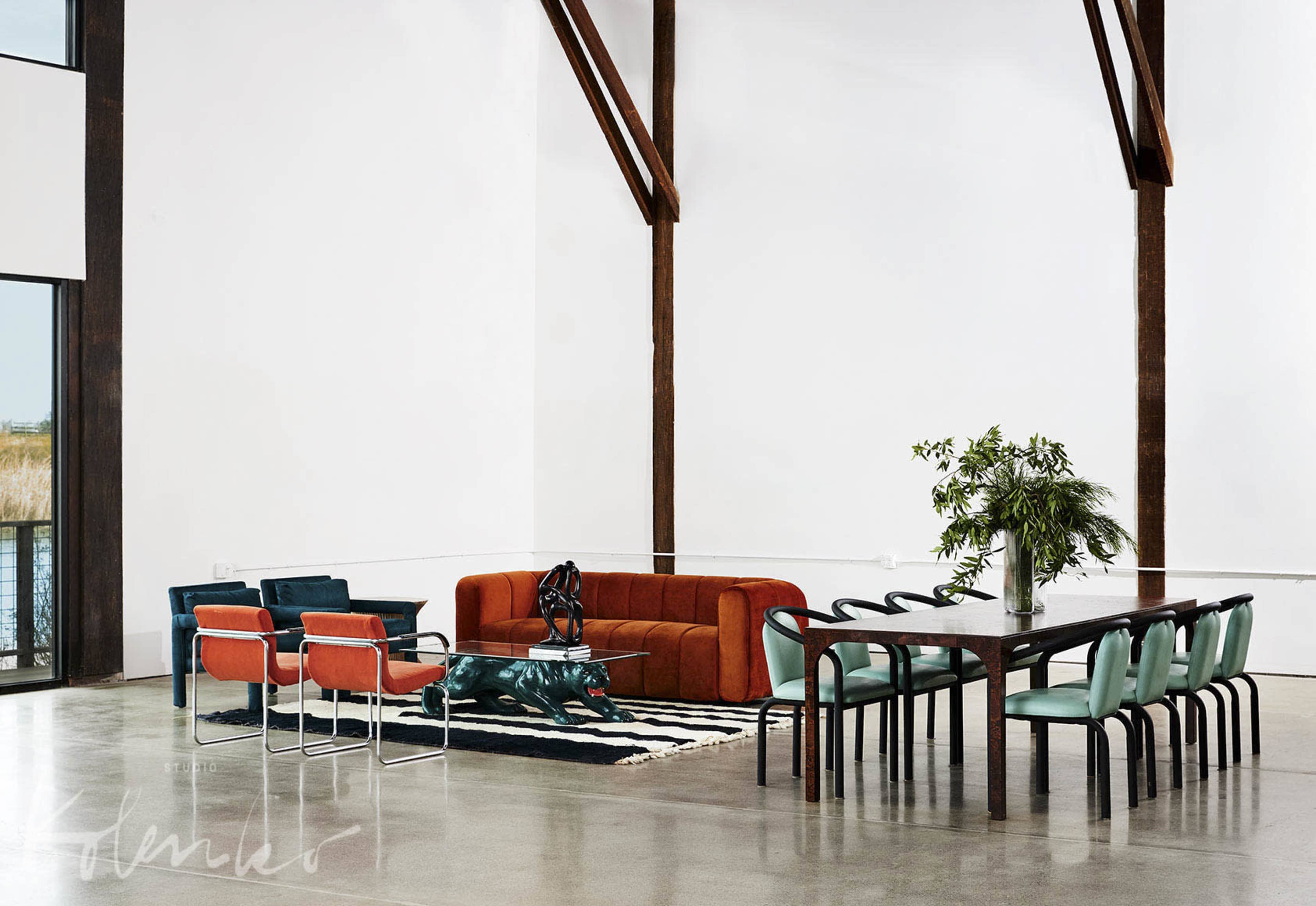 A spacious interior with a large dining table, colorful chairs, a modern couch, and a decorative rug.
