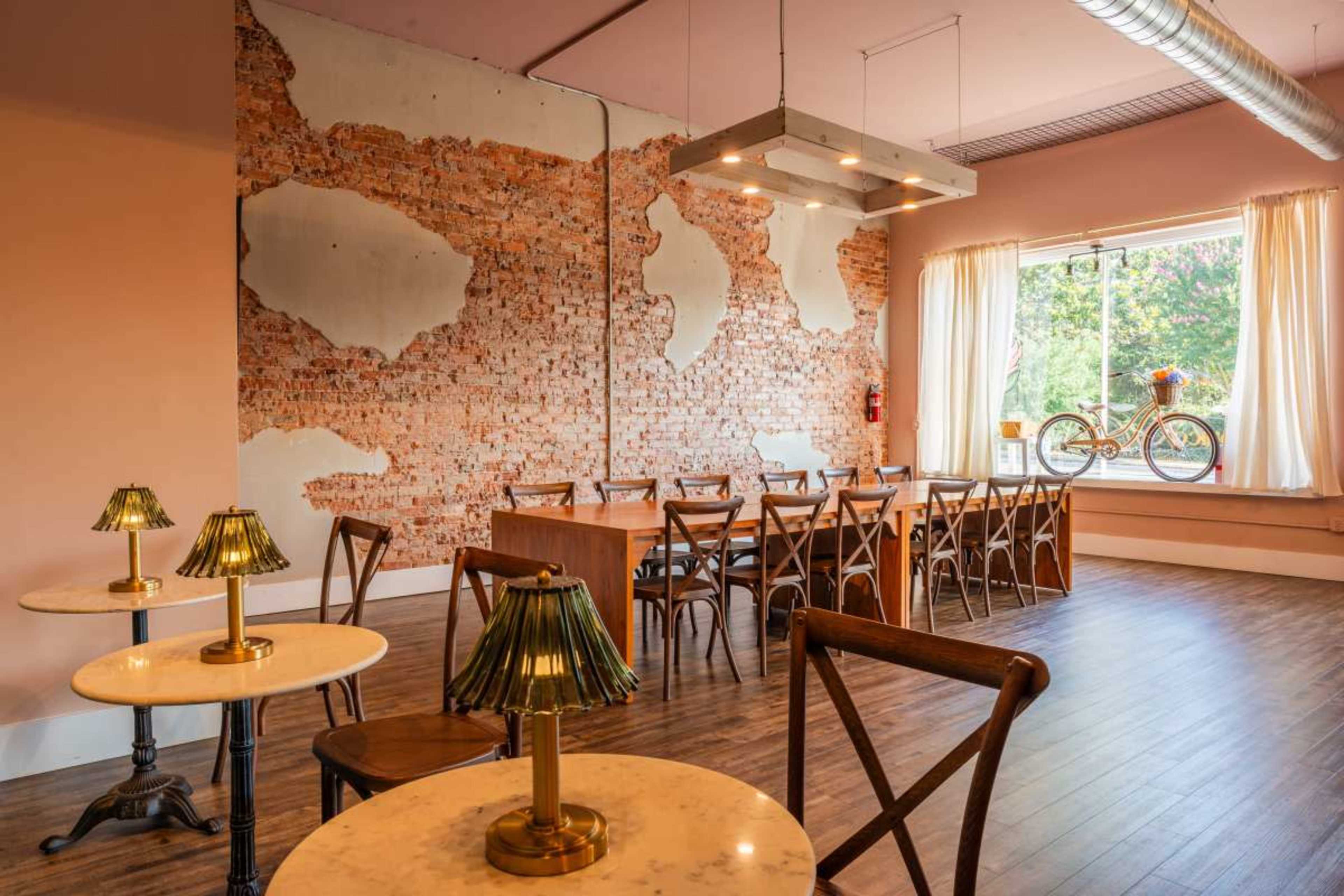 The image shows a contemporary interior space featuring wooden furniture, a brick wall, and a large window with a bicycle displayed outside.