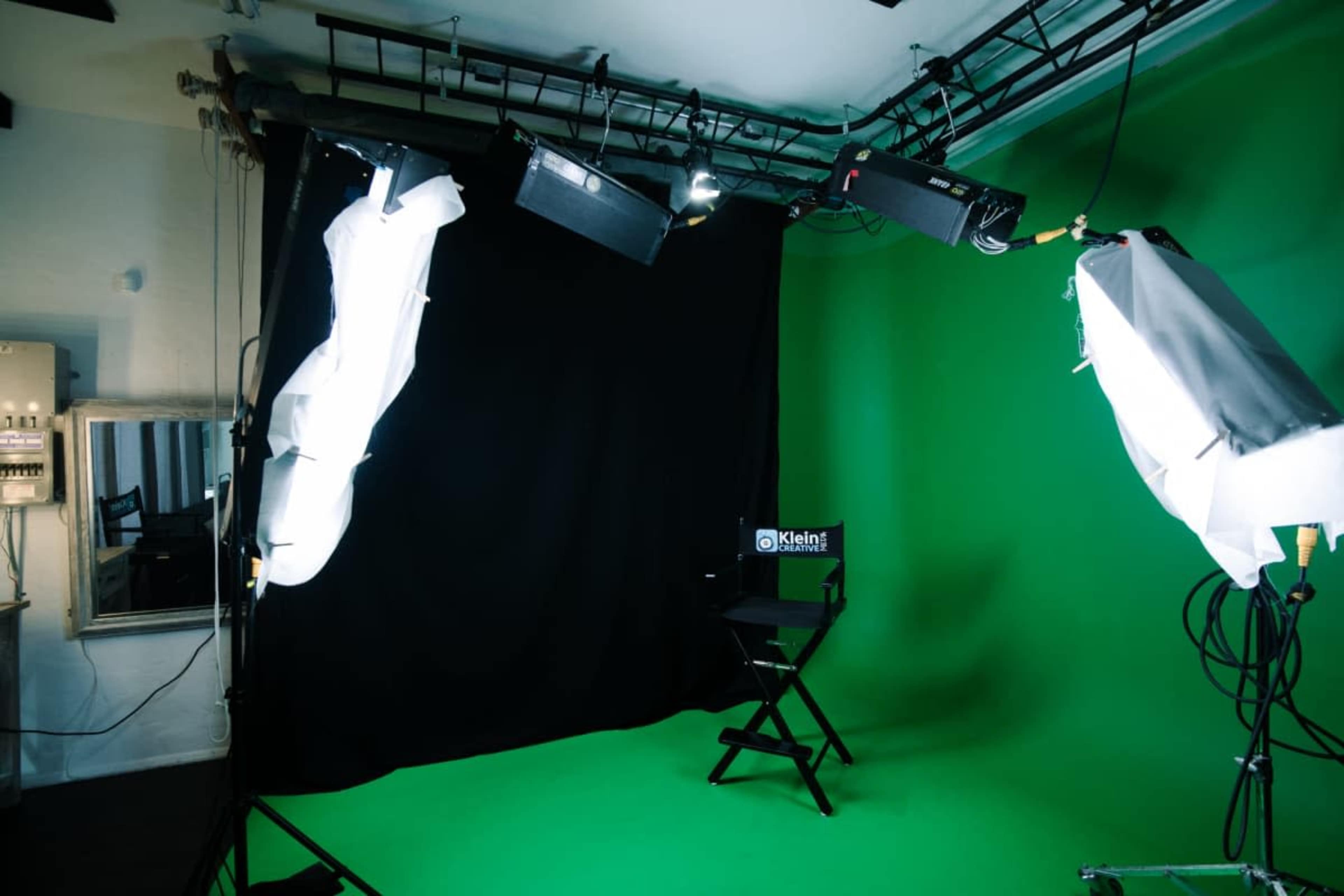 The image shows a photography studio with a green screen backdrop, lighting equipment, and a director's chair.