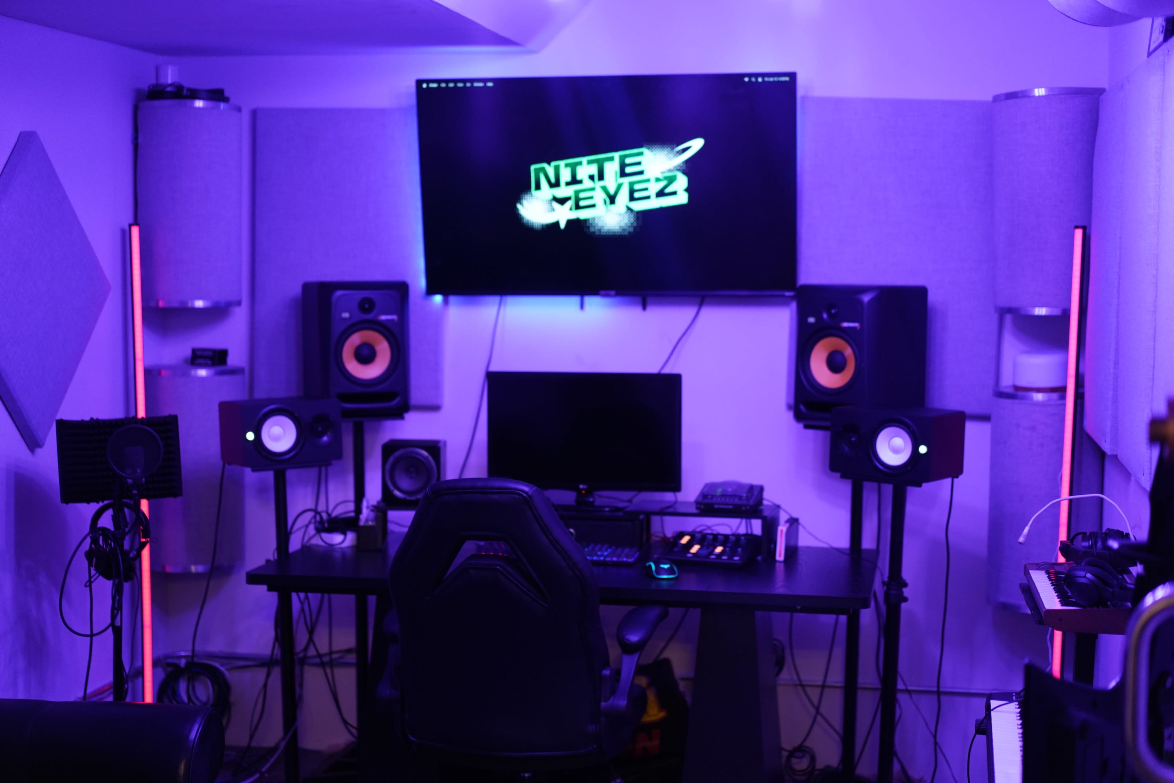 The image shows a home recording studio with a computer desk, speakers, and soundproofing materials, illuminated by purple lighting.