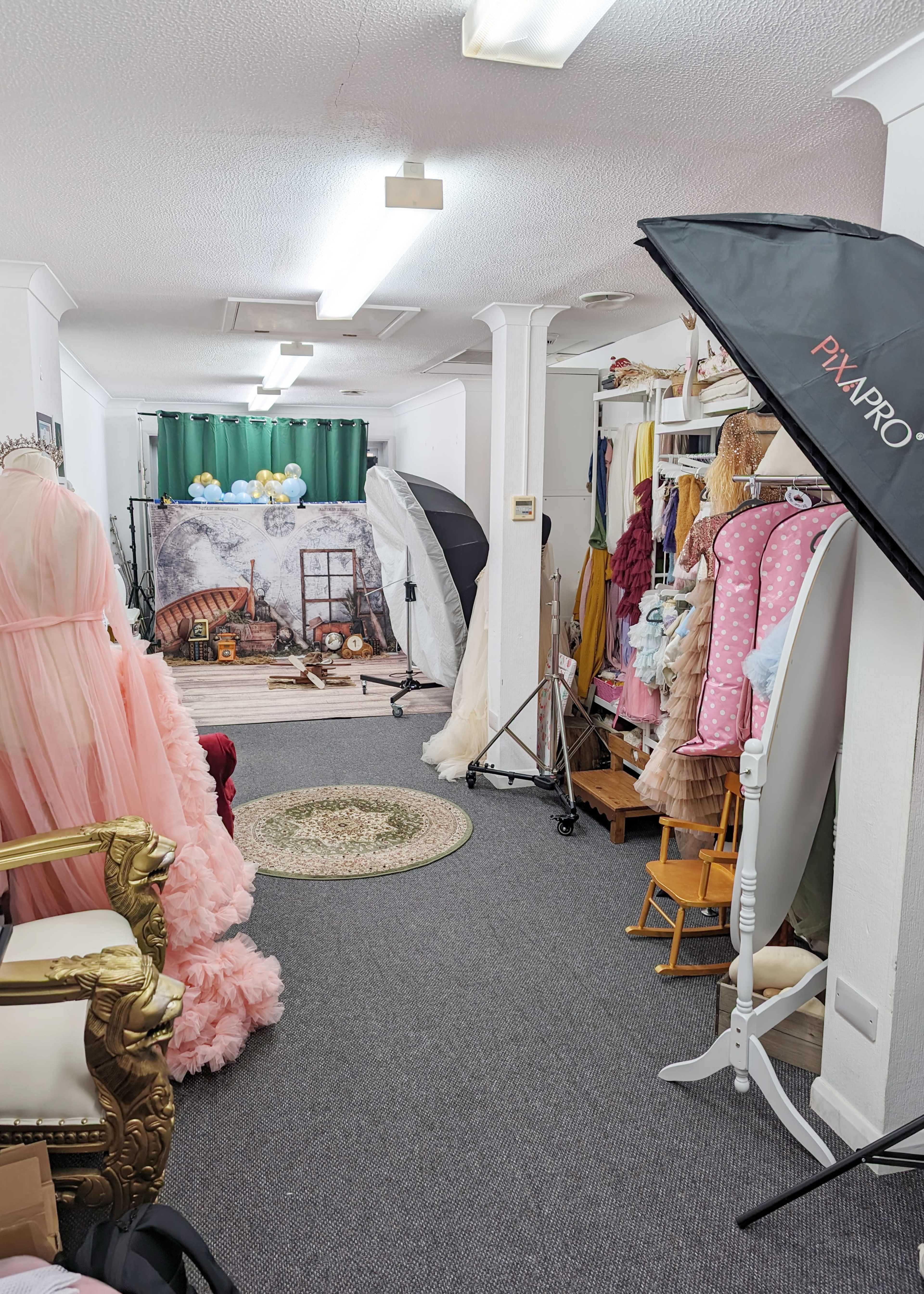 A photography studio featuring a decorative backdrop, multiple lighting equipment, and racks of clothing, set in a carpeted space.