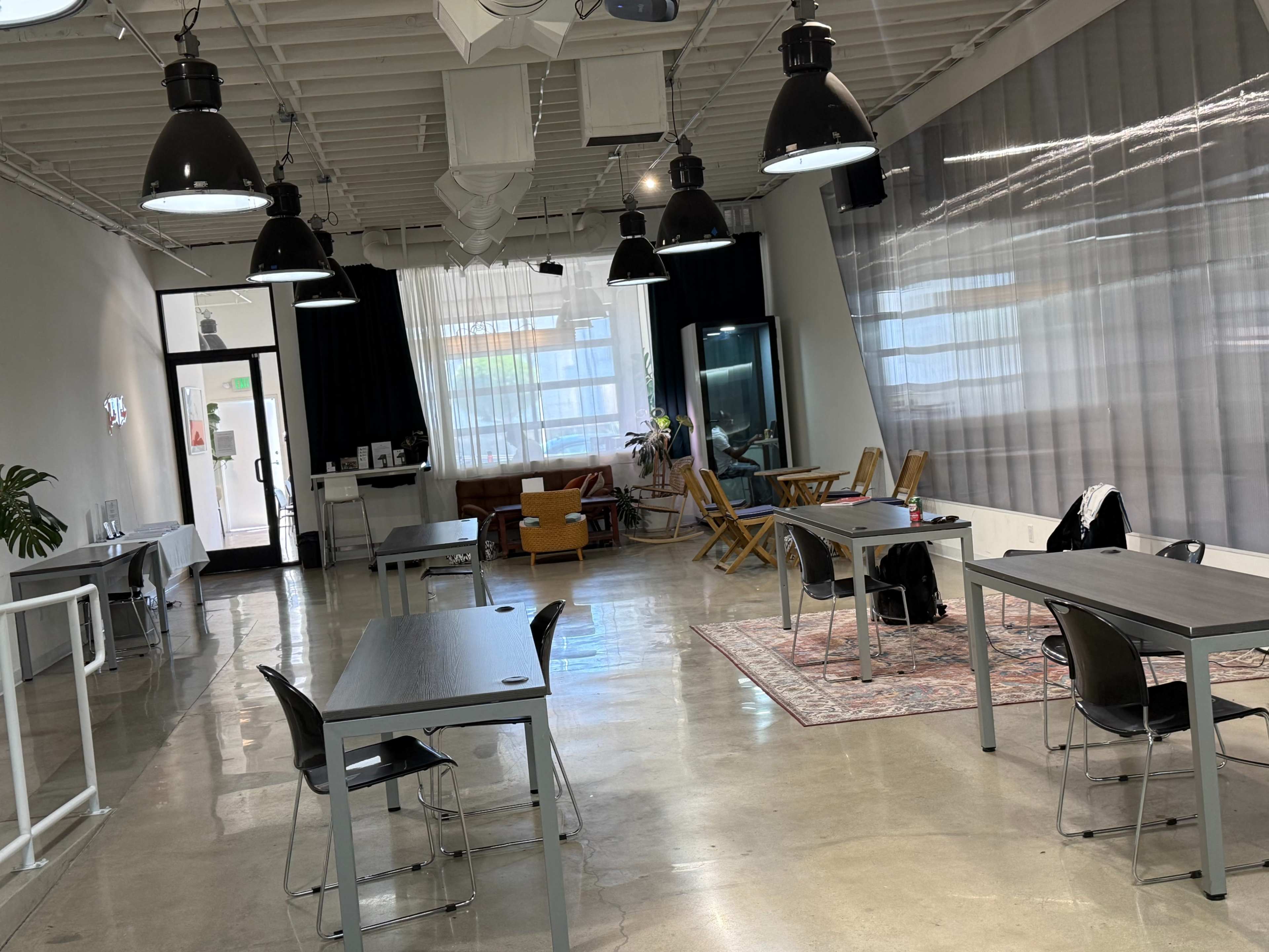 The image shows a bright, modern coworking space with desks, chairs, and a lounge area featuring a sofa.