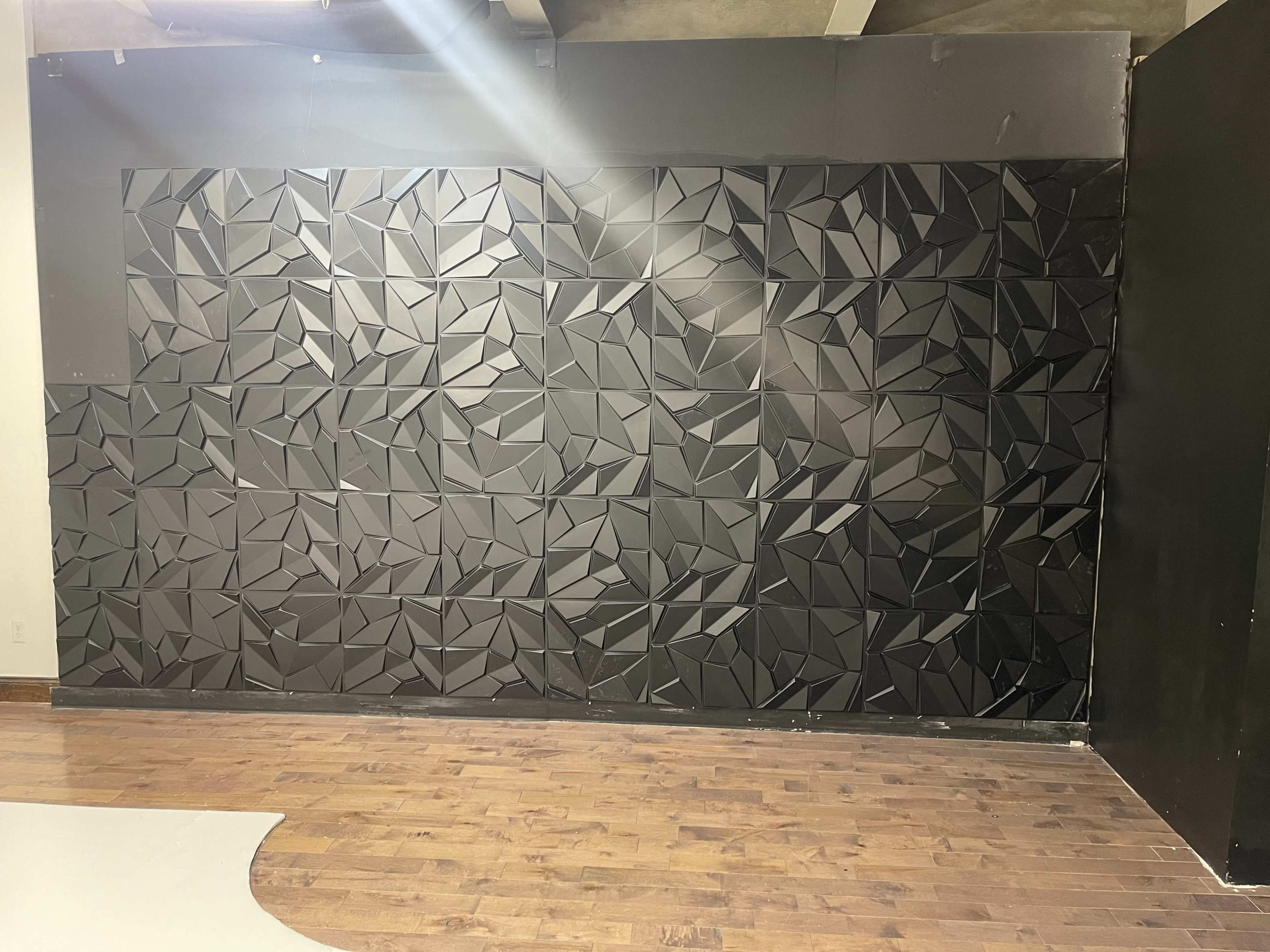 A textured black wall featuring a geometric pattern of angular shapes, with a wooden floor in the foreground.