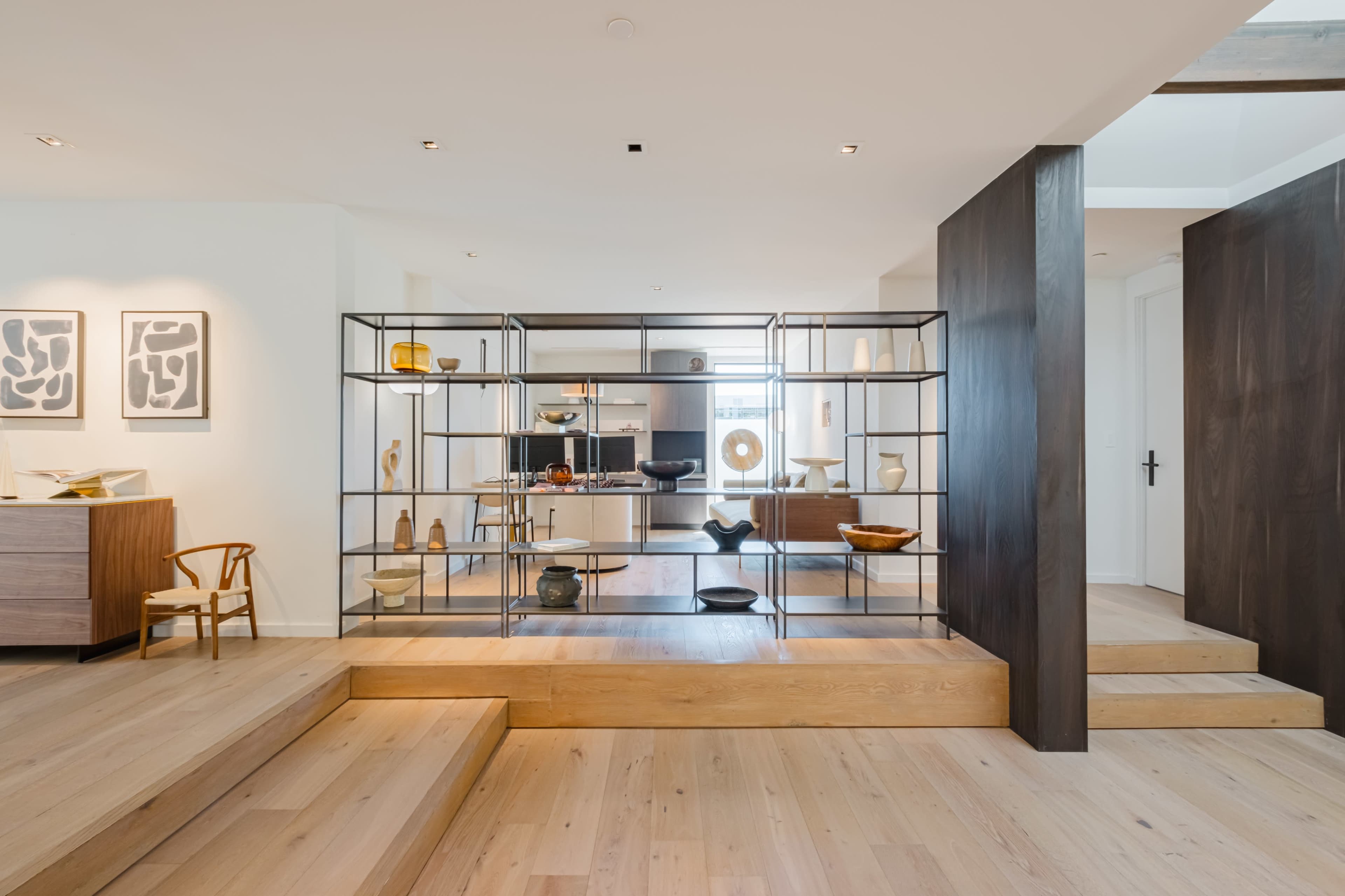 A modern interior space featuring a display shelf with various decorative items, steps leading to another level, and a minimalistic design.