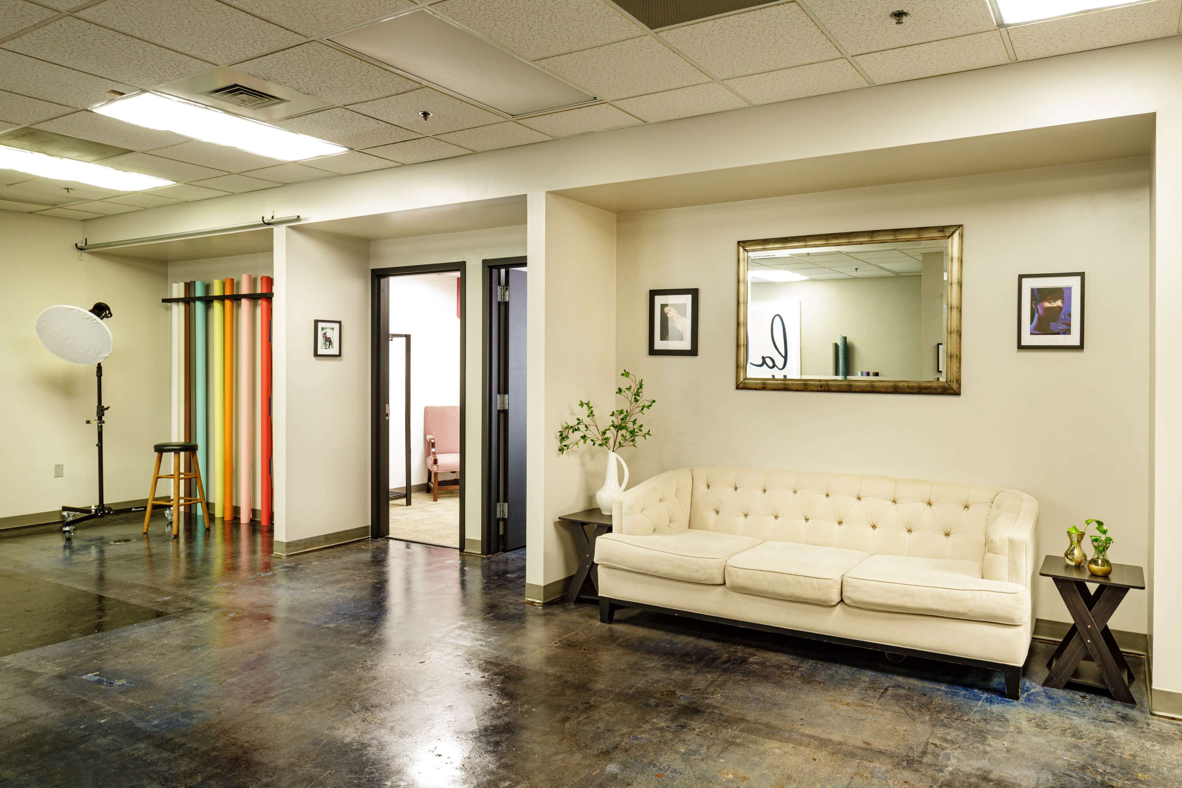 A spacious, well-lit studio interior featuring a cream-colored sofa, a colorful backdrop, and a standing light source.