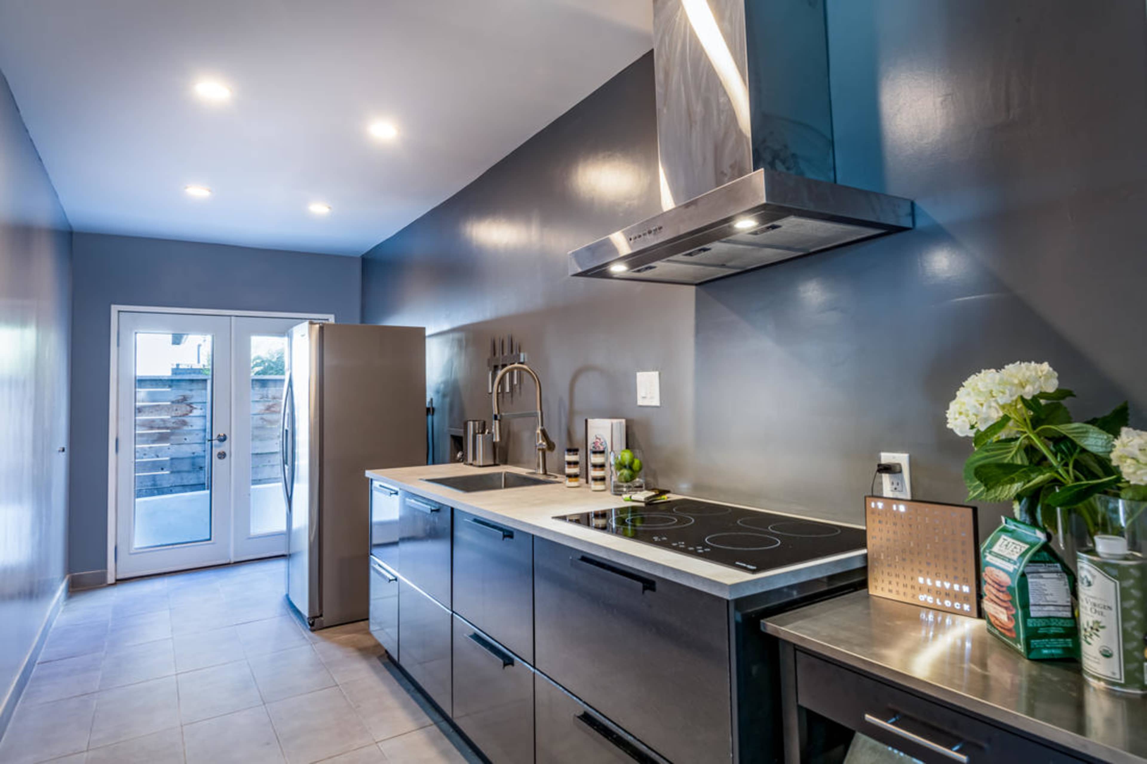 The kitchen features stainless steel cabinetry, a modern cooktop, and a door leading to an outdoor area.