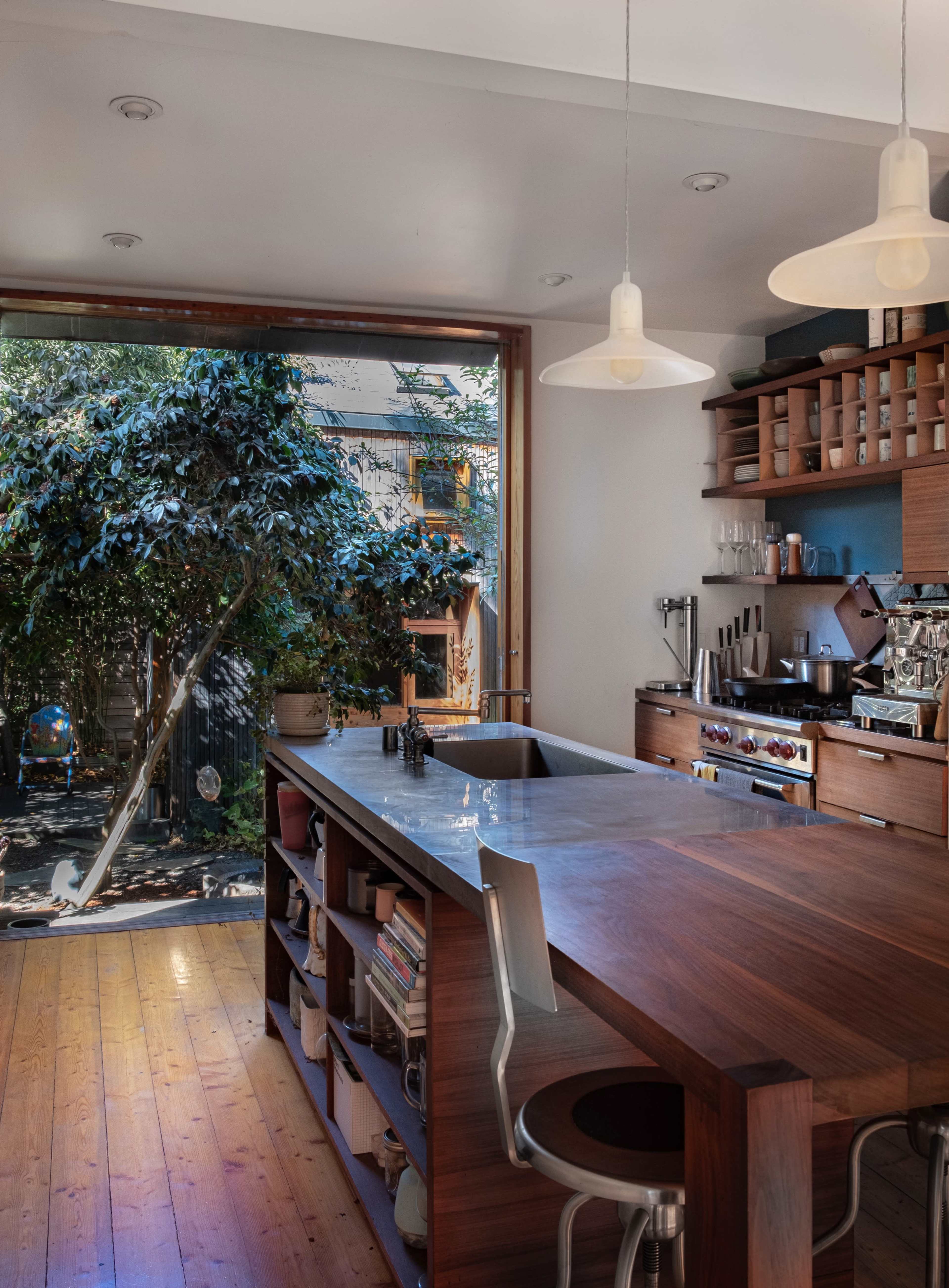 A modern kitchen with a wooden island, stainless steel appliances, and a large window that opens to a garden view.