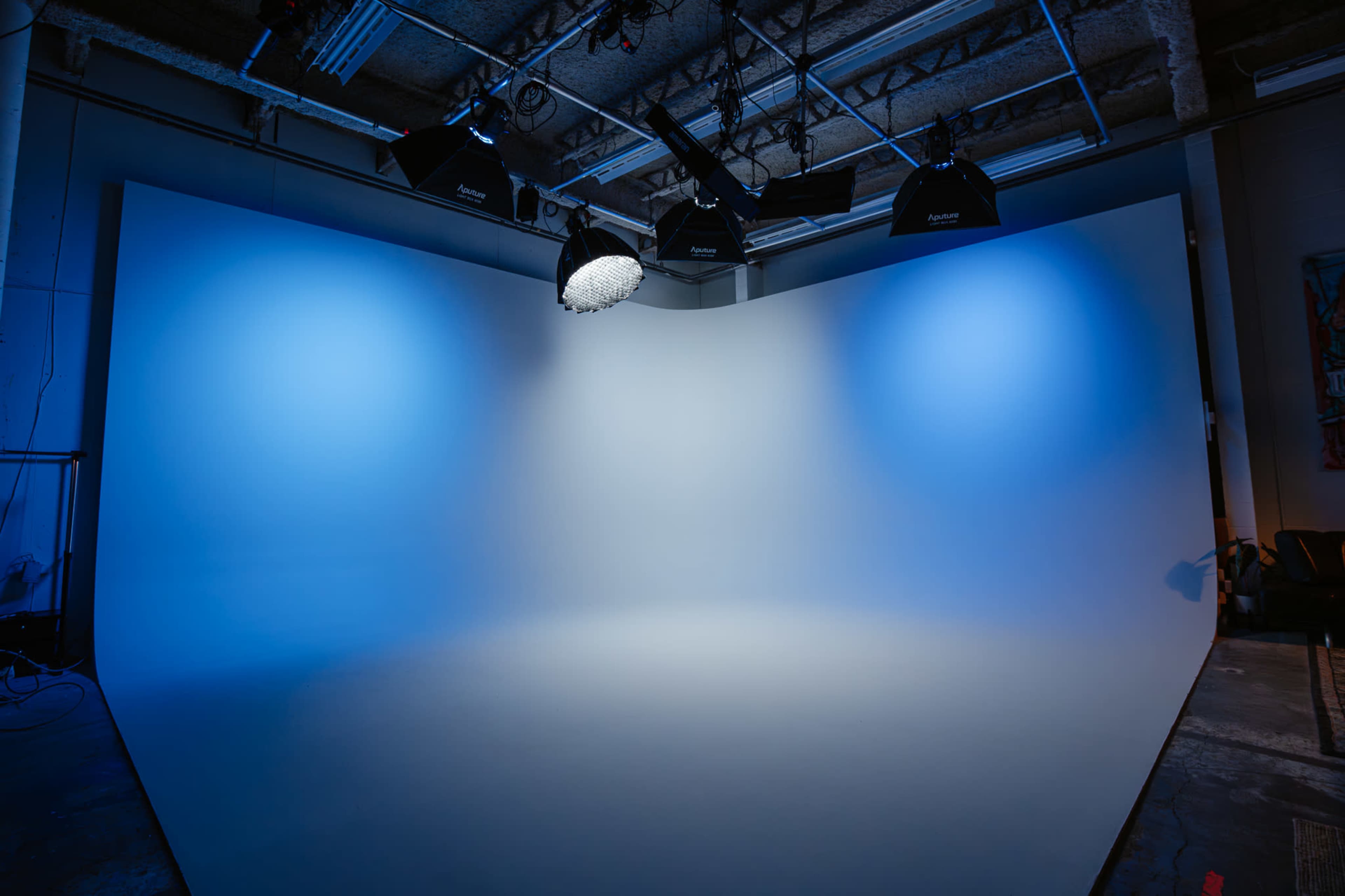 The image shows a photography studio with a curved backdrop and blue lighting from overhead softboxes.