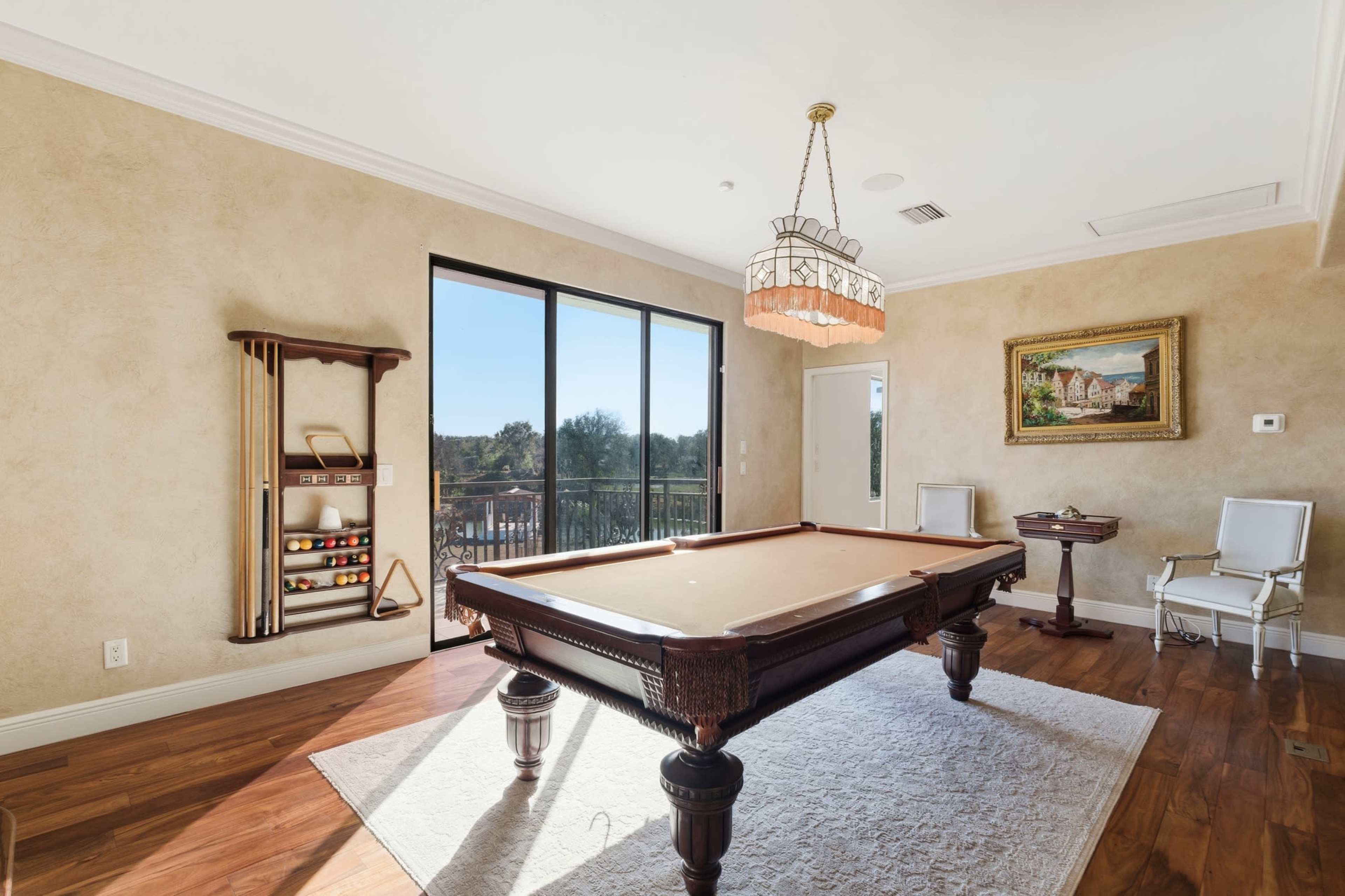 The room features a billiard table in the center, surrounded by large windows that allow natural light to fill the space.