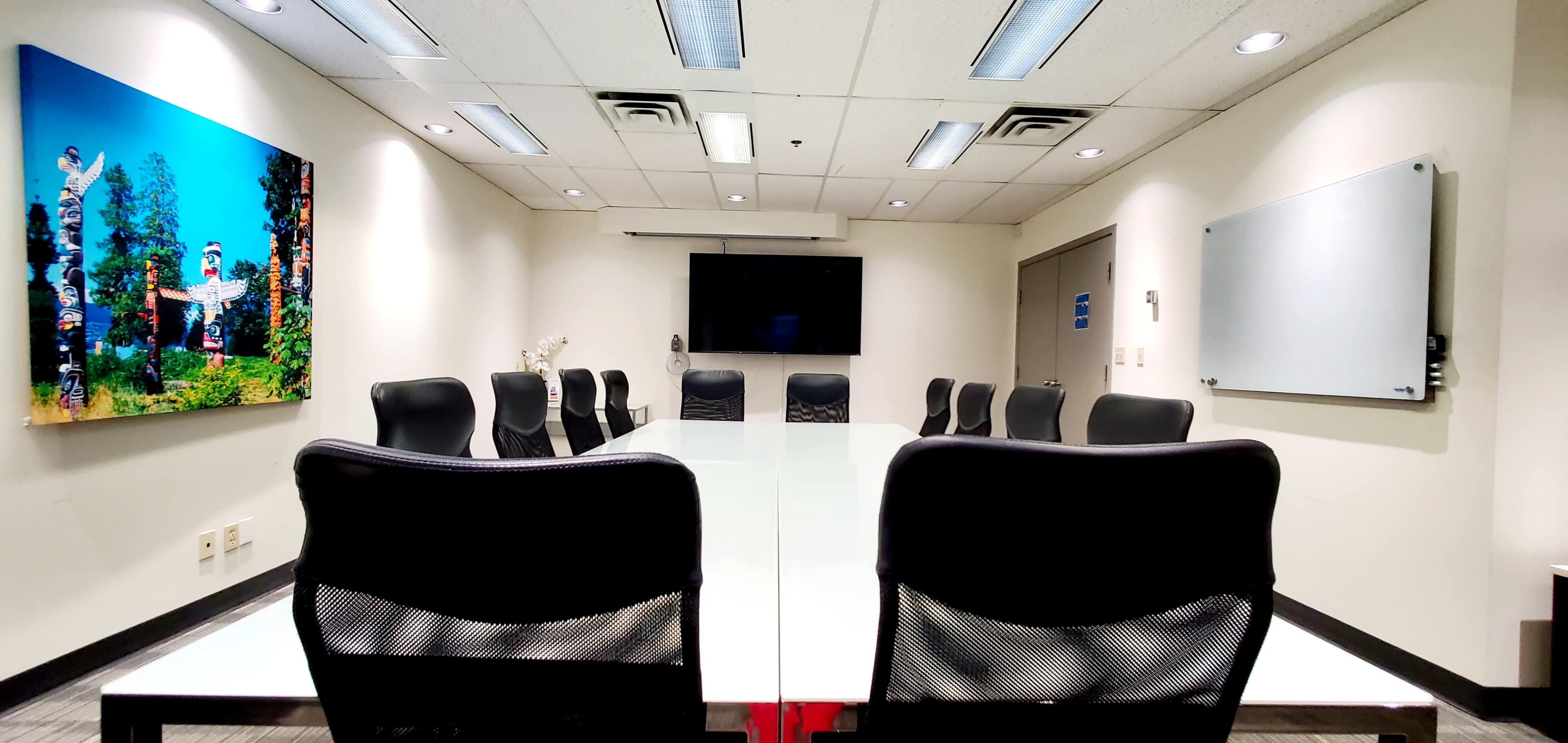 A modern conference room features a long glass table, black chairs, a large screen, and a mural of trees on one wall.