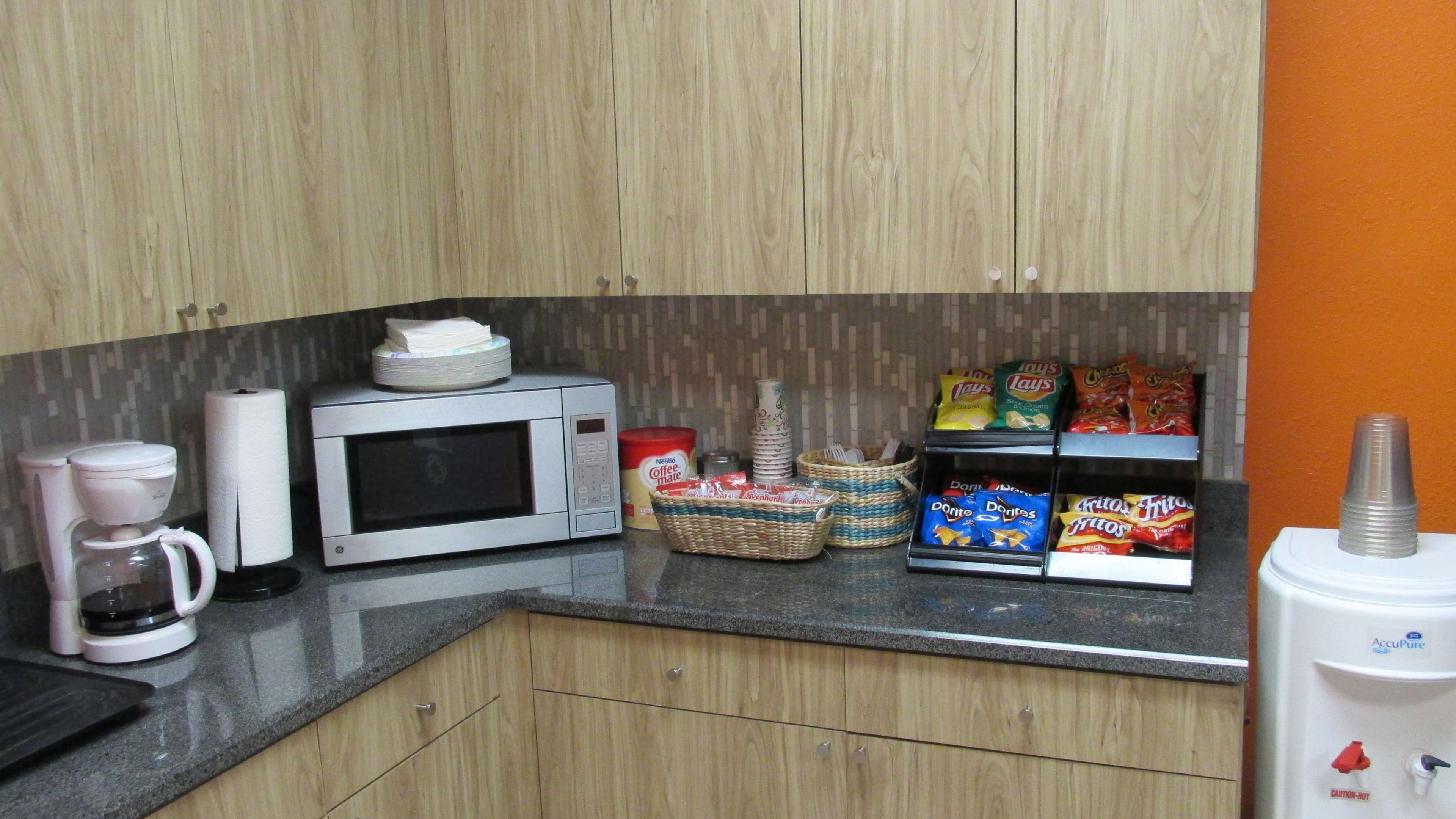 A kitchen countertop features a microwave, coffee maker, and a basket of snacks next to a mini fridge.