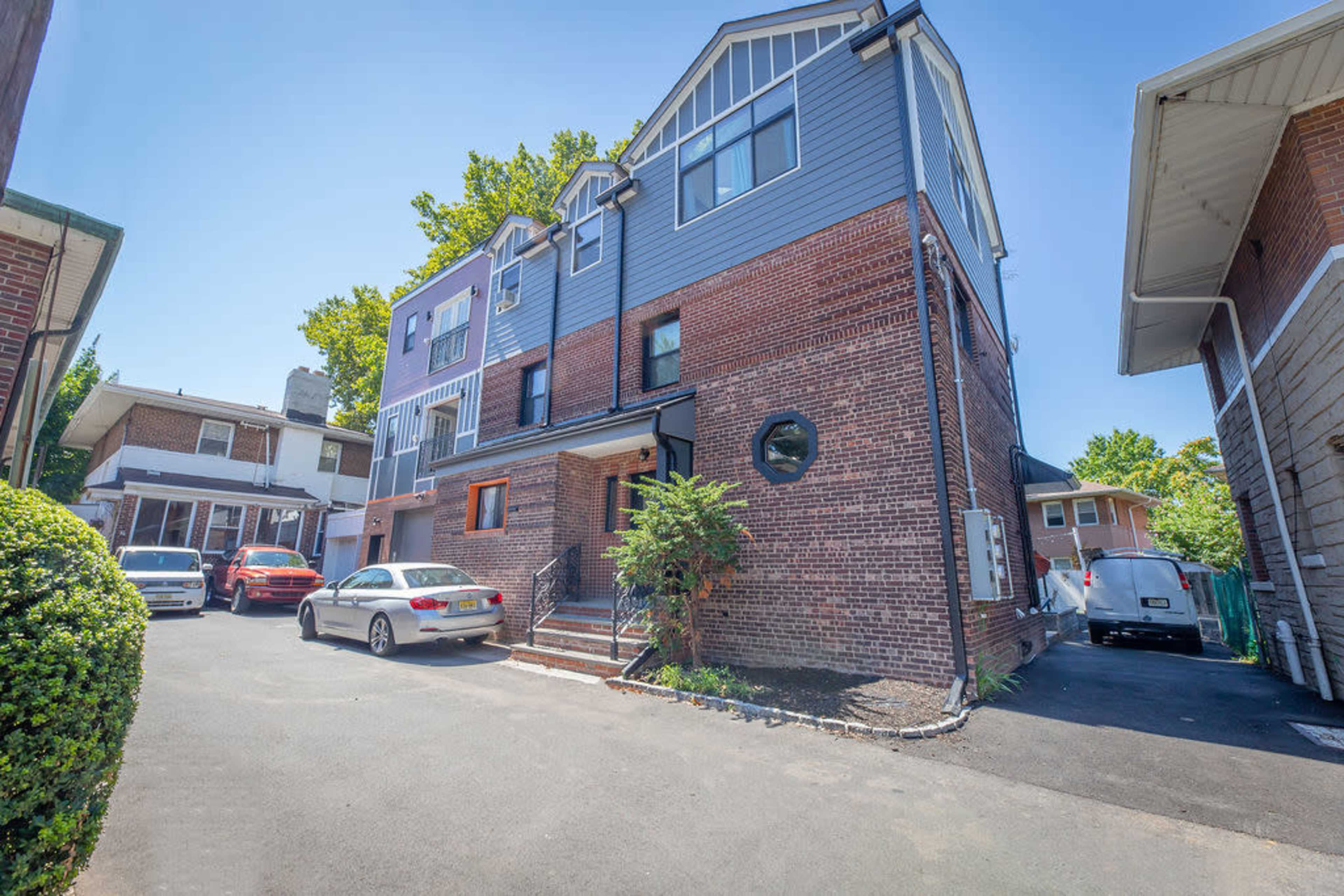 A multi-story brick and gray-clad residential building situated next to a paved driveway with parked cars.