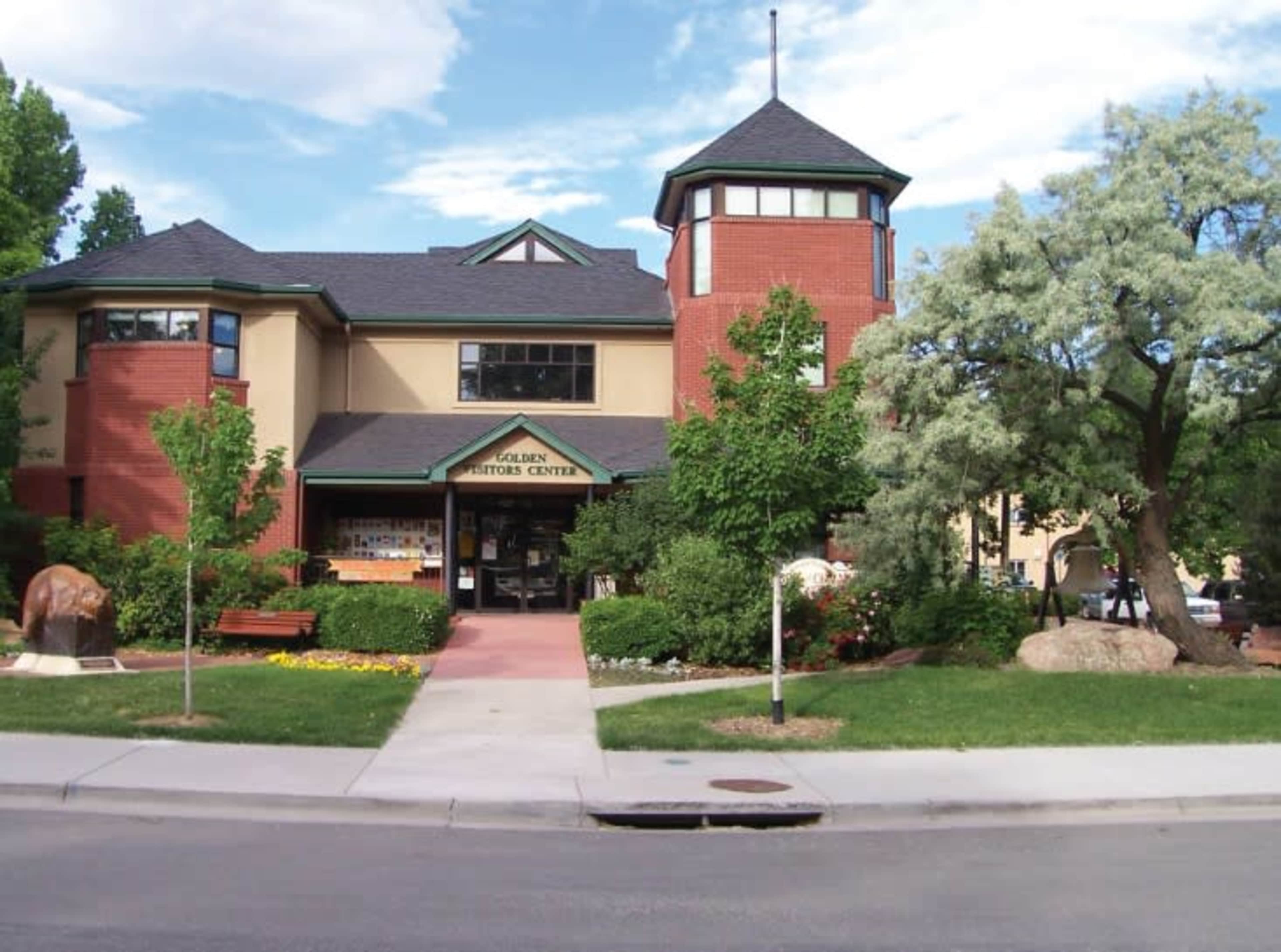 A two-story visitor center with a brick and stucco exterior, surrounded by greenery and featuring a small sculpture of a bear in front.