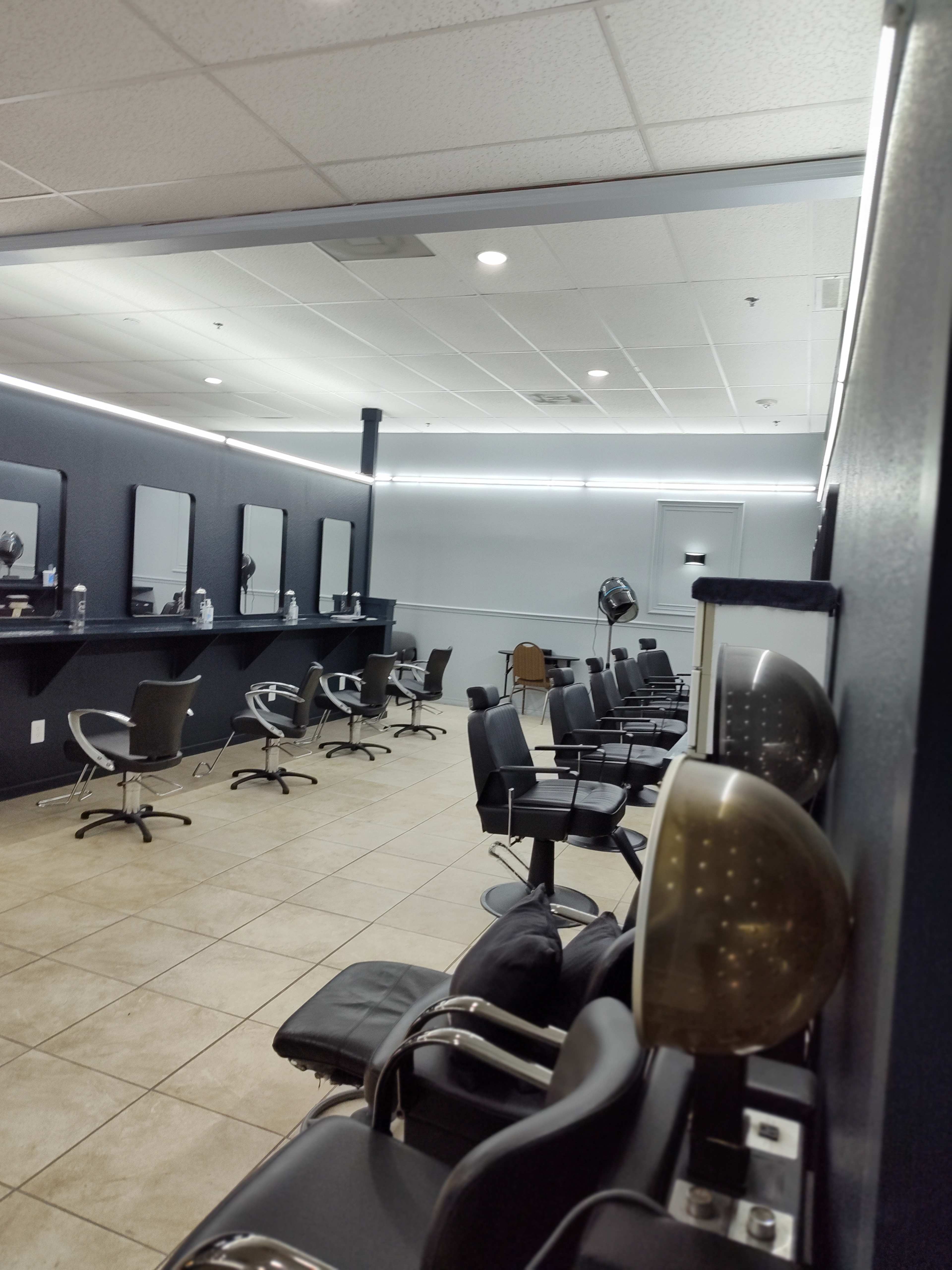 A modern hair salon with several styling stations, mirrors, and black chairs arranged along the walls.