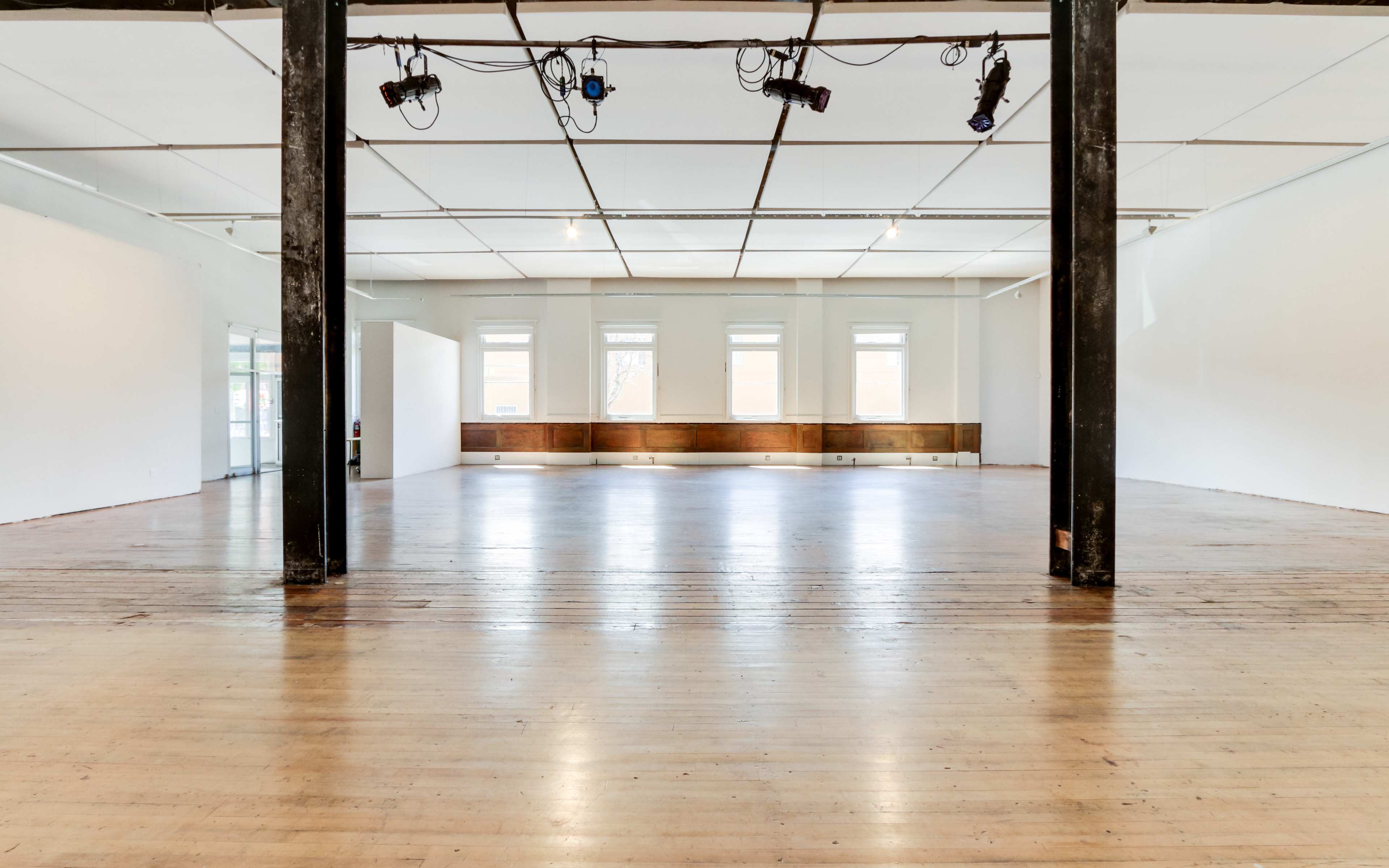 A large, empty room with wooden floors, tall windows, and exposed beams.