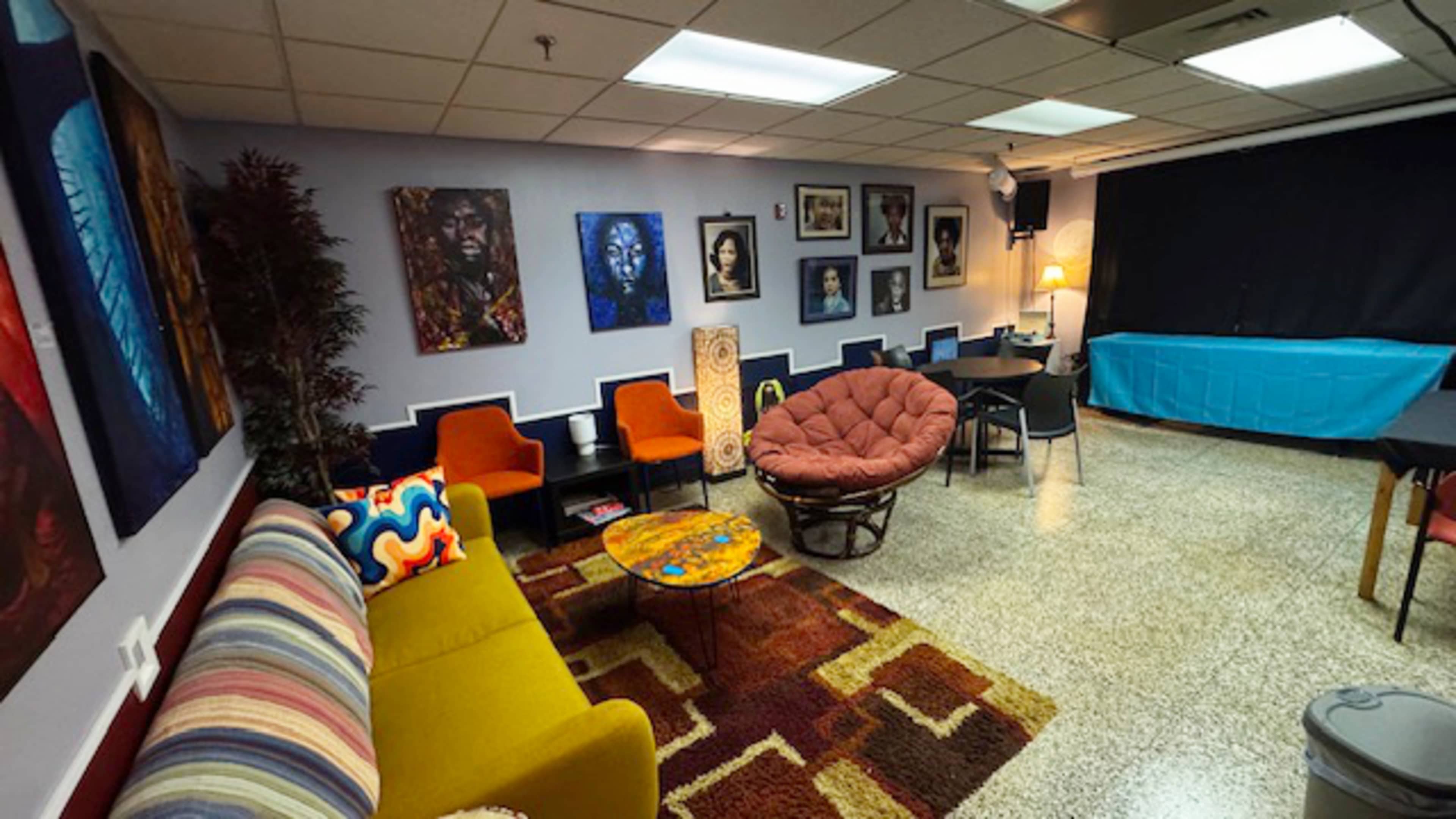 The room features colorful seating, a patterned rug, and walls adorned with various framed artworks.