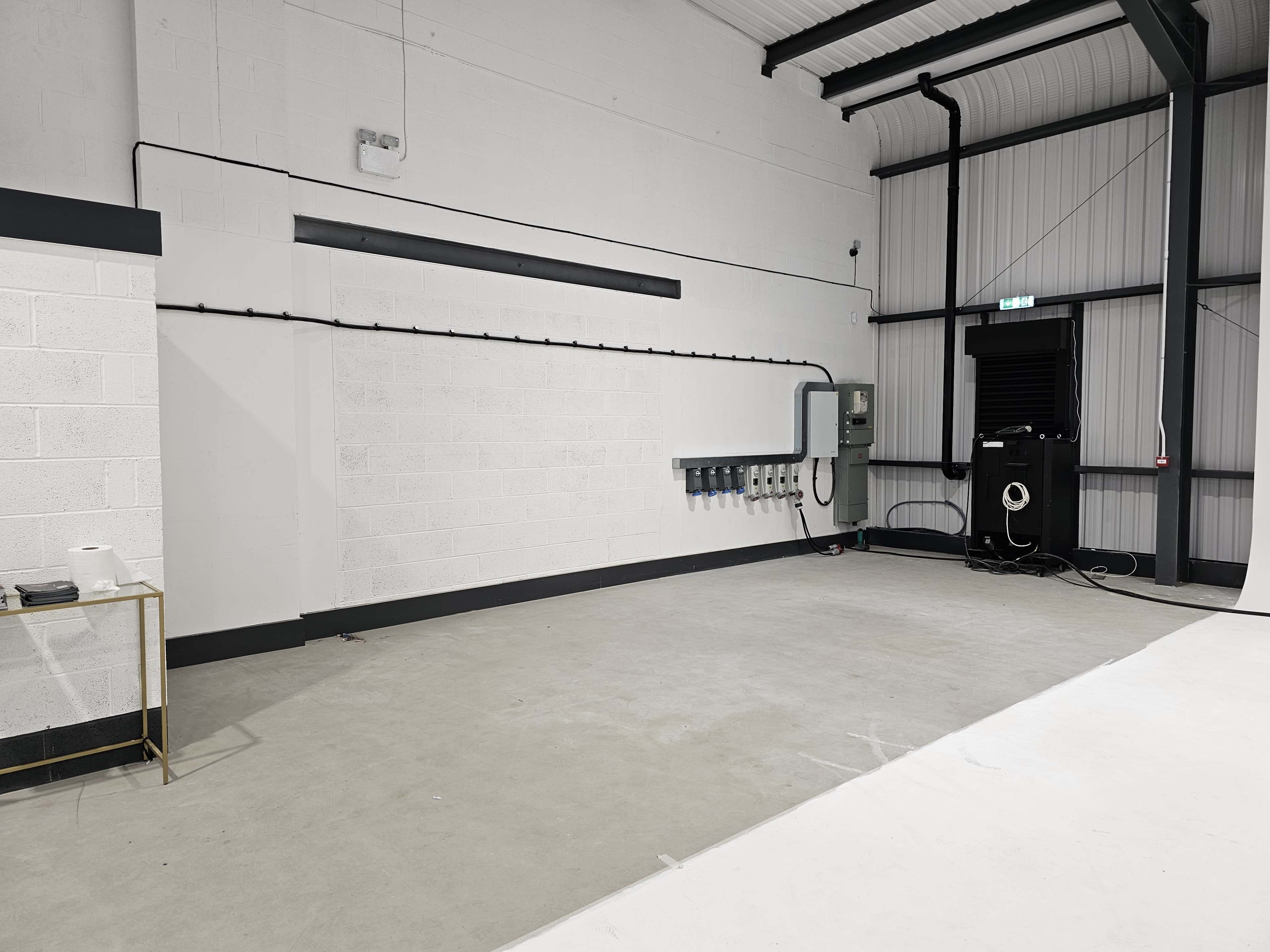An empty industrial space with a concrete floor, a white wall, and electrical panels mounted on the wall.