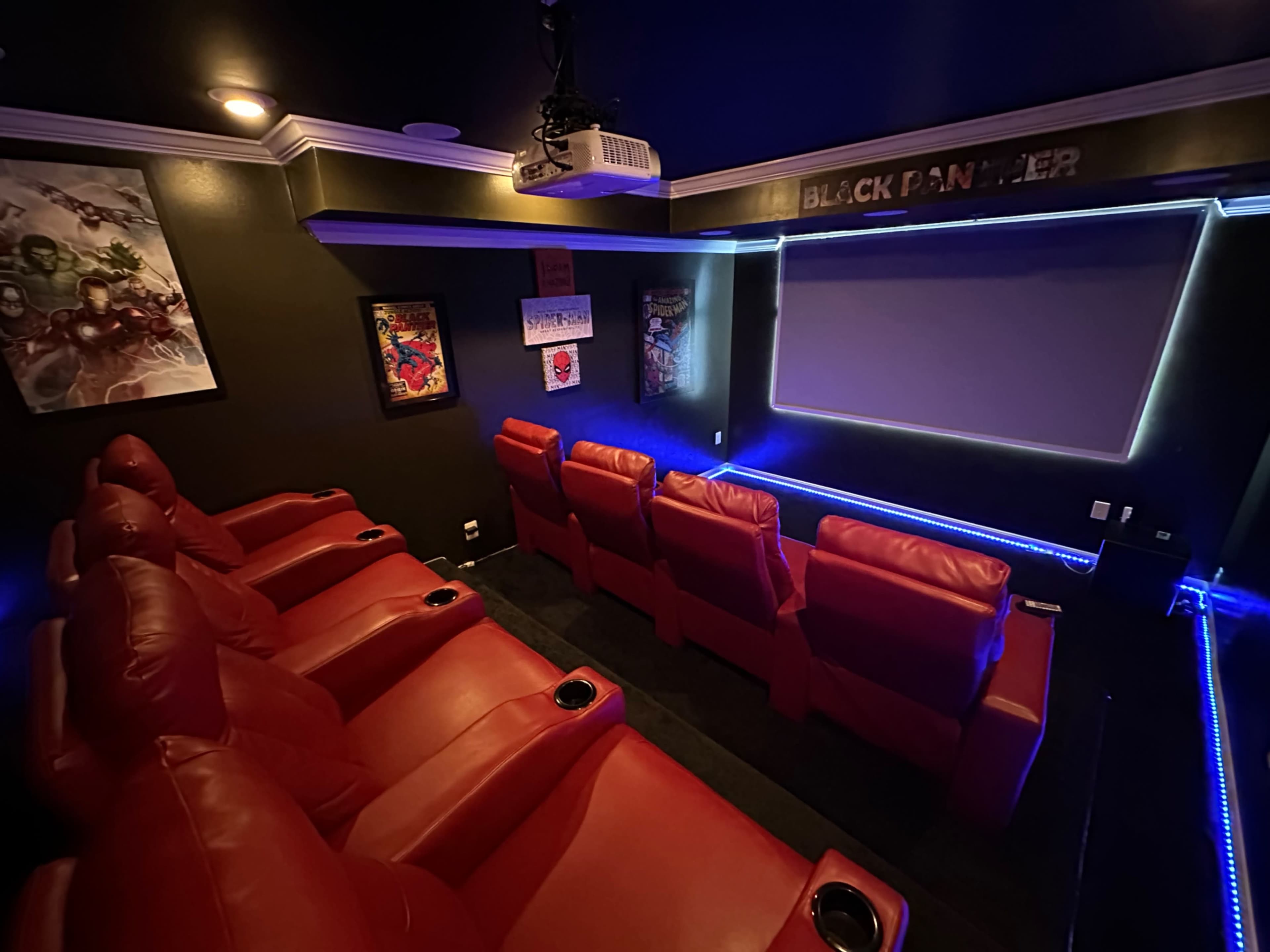 A home theater with red recliner seating, a large movie screen, and superhero-themed artwork on the walls.