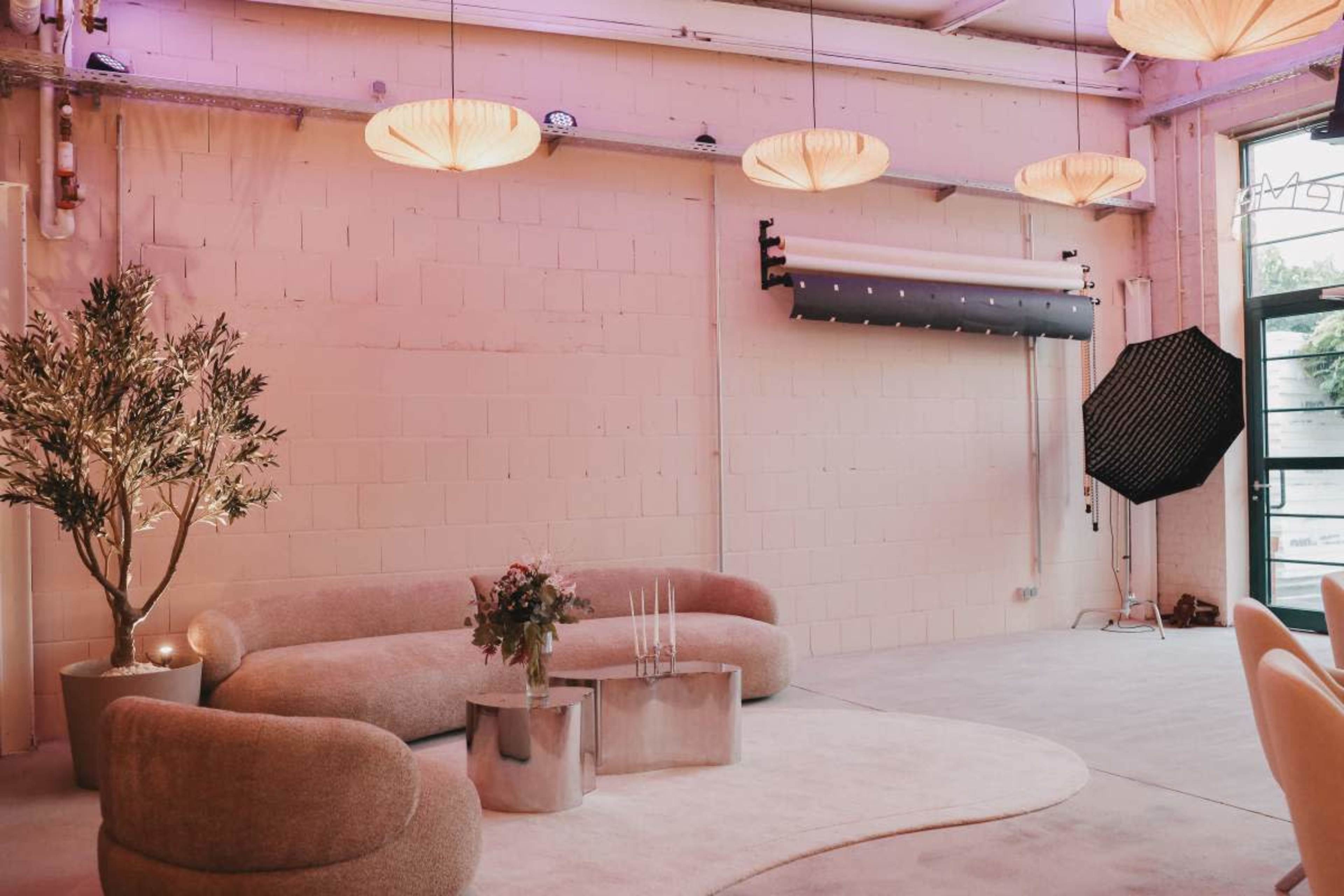 The image shows a modern, minimalist interior with a curved sofa and armchair, a round coffee table, and large pendant lights hanging from the ceiling.