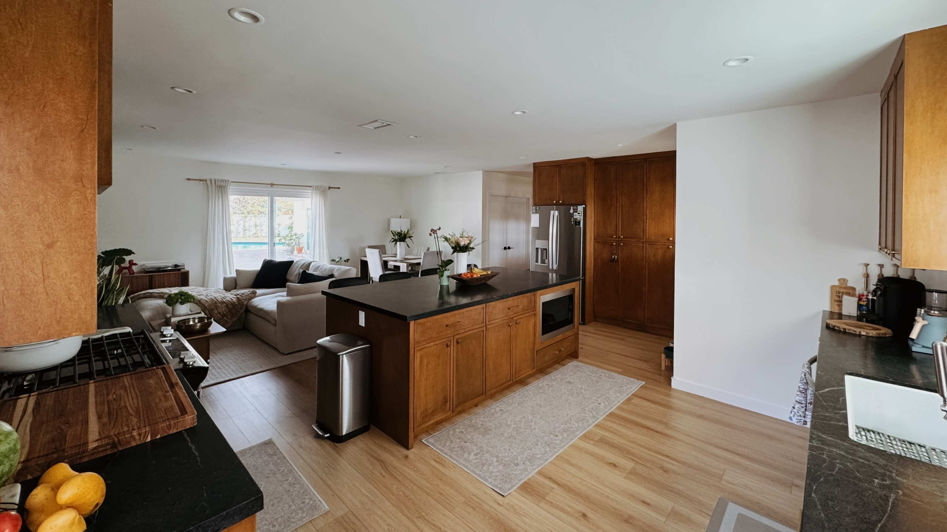 A modern kitchen opens into a bright living area, featuring wooden cabinetry, a central island, and a comfortable seating area.
