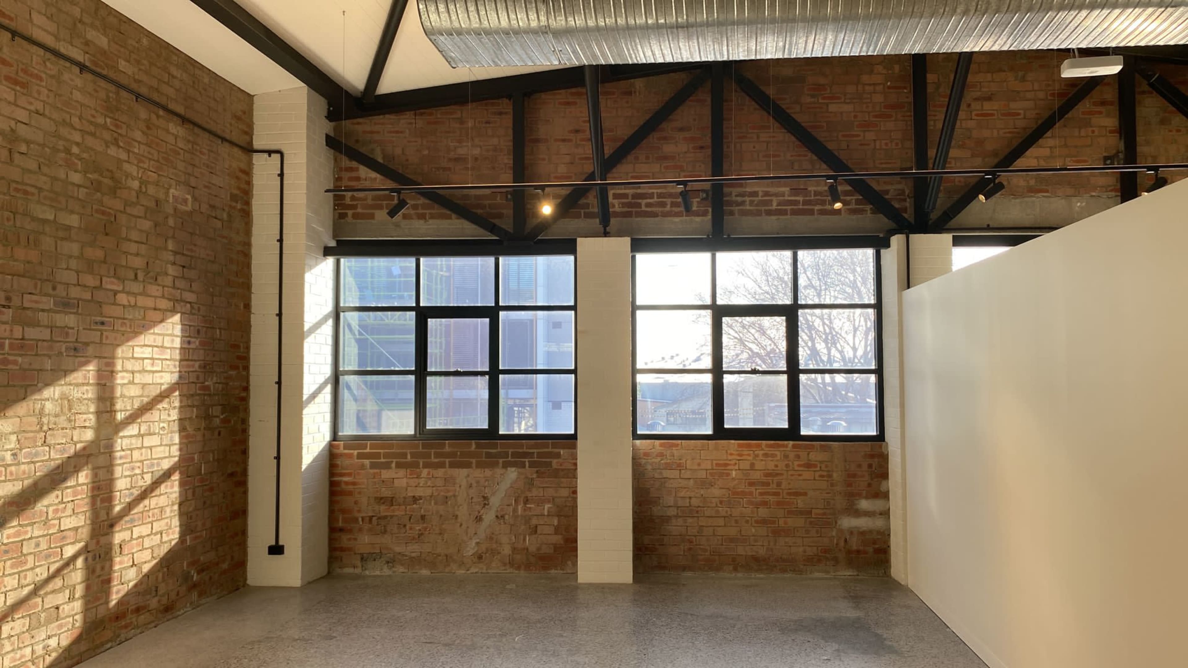 An interior space with exposed brick walls, large windows providing natural light, and a white partition.
