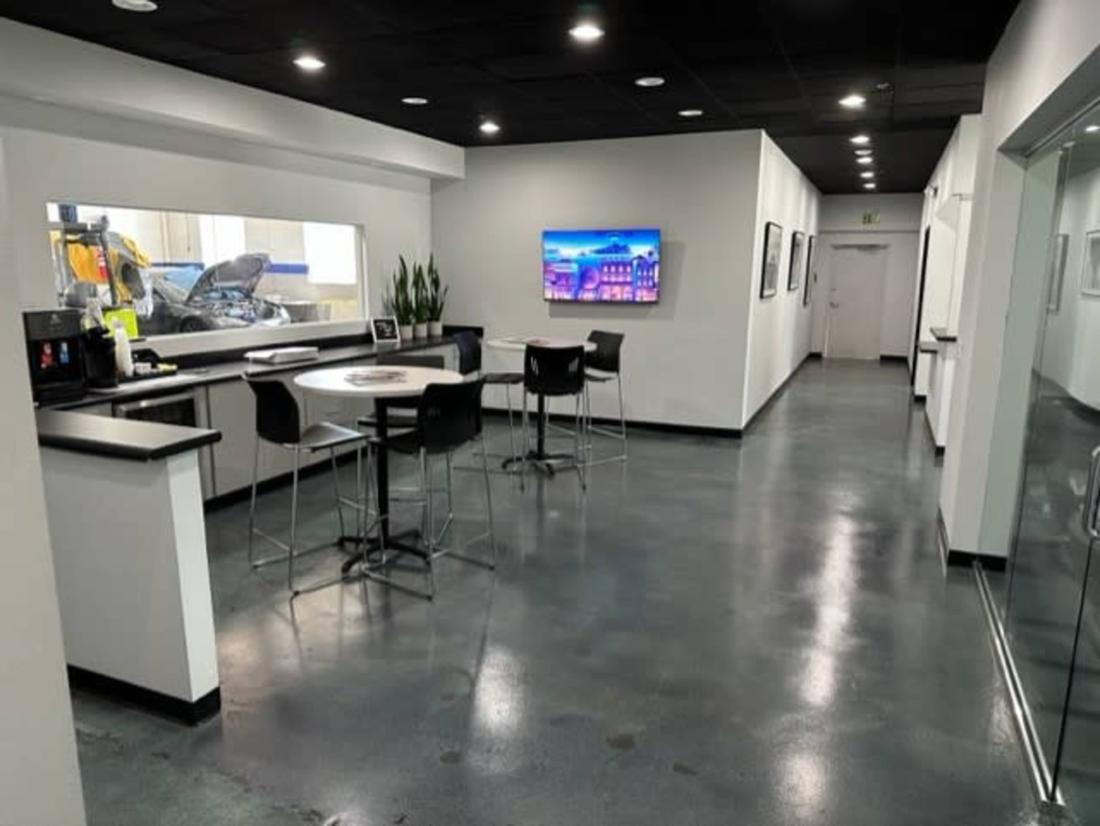 A modern interior of an office space with a long corridor, tables and chairs, and a television on the wall.